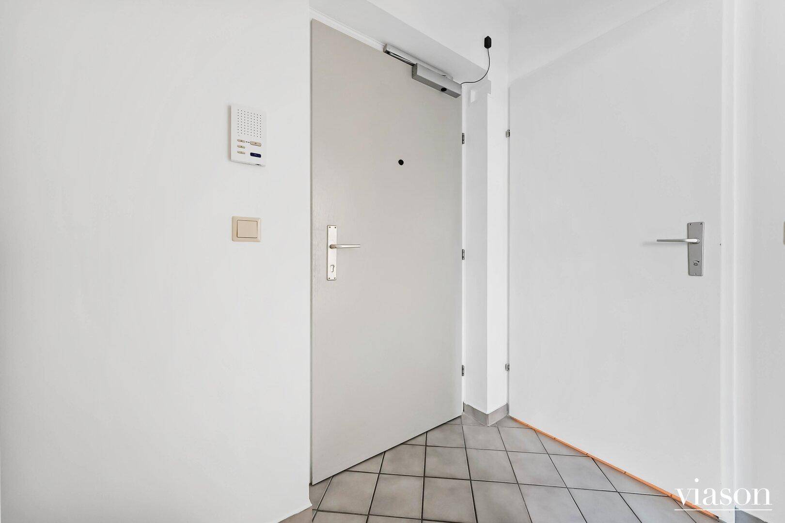 Heller Flur mit Fliesenboden und einer Gegensprechanlage an der Wand.