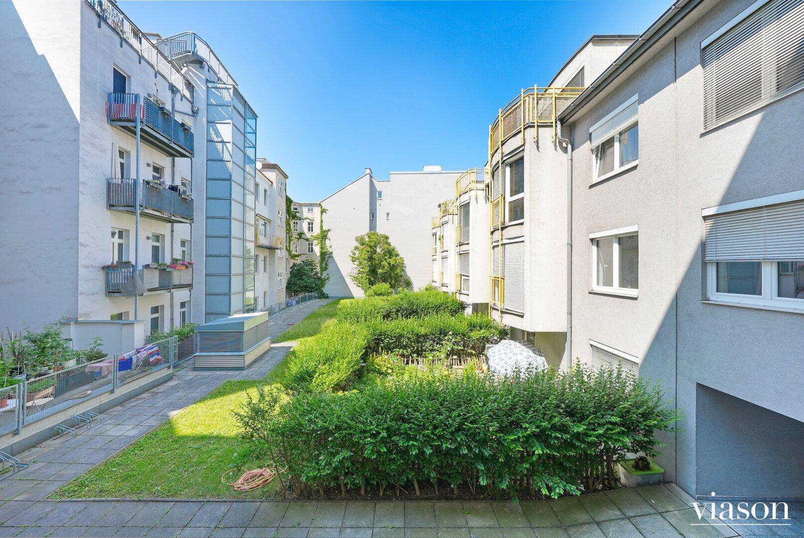 Innenhof mit Rasenfläche und Hecken, umgeben von Wohngebäuden mit modernen Fassaden.