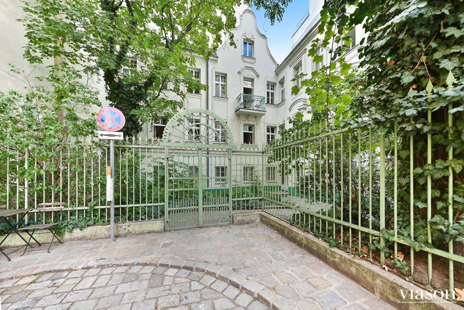 Innenhof mit schmiedeeisernem Tor und grünen Pflanzen, umgeben von historischen Gebäuden.
