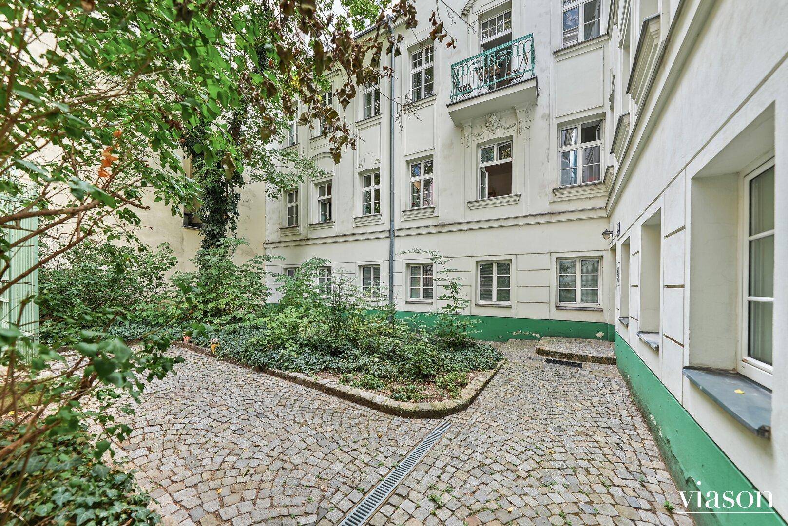 Begrünter Innenhof mit Kopfsteinpflaster und üppiger Vegetation, umgeben von Altbauten.