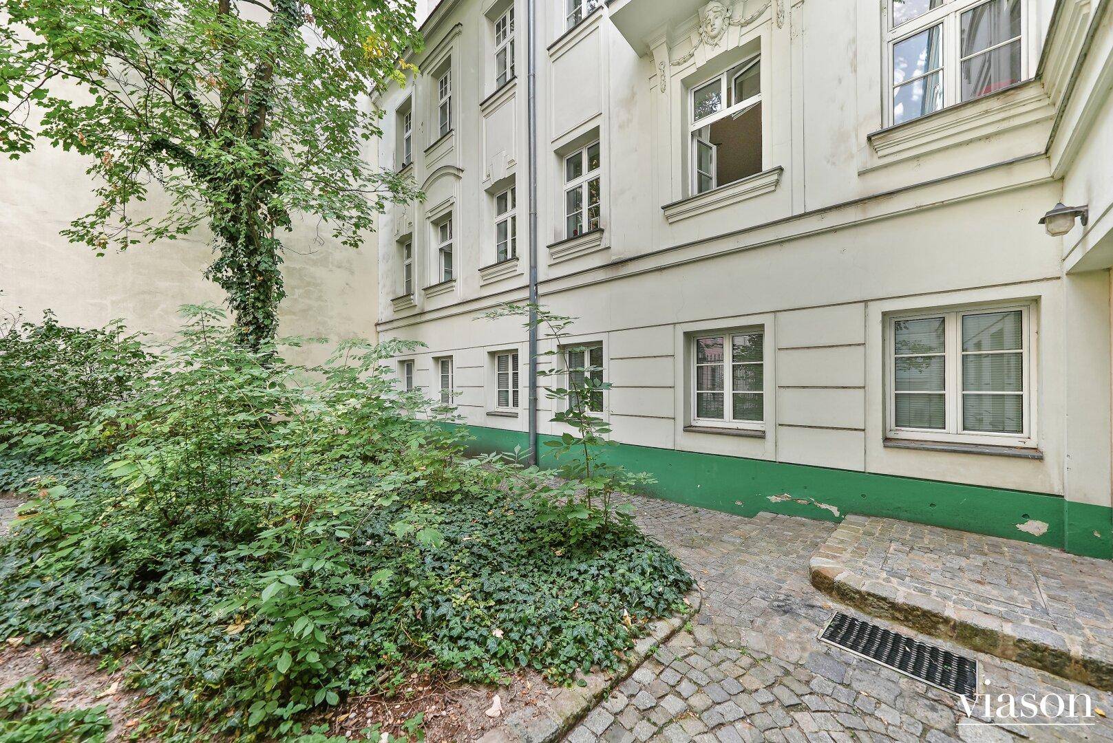 Ruhiger Innenhof mit viel Grün und Kopfsteinpflaster, umgeben von der Gebäudefassade.