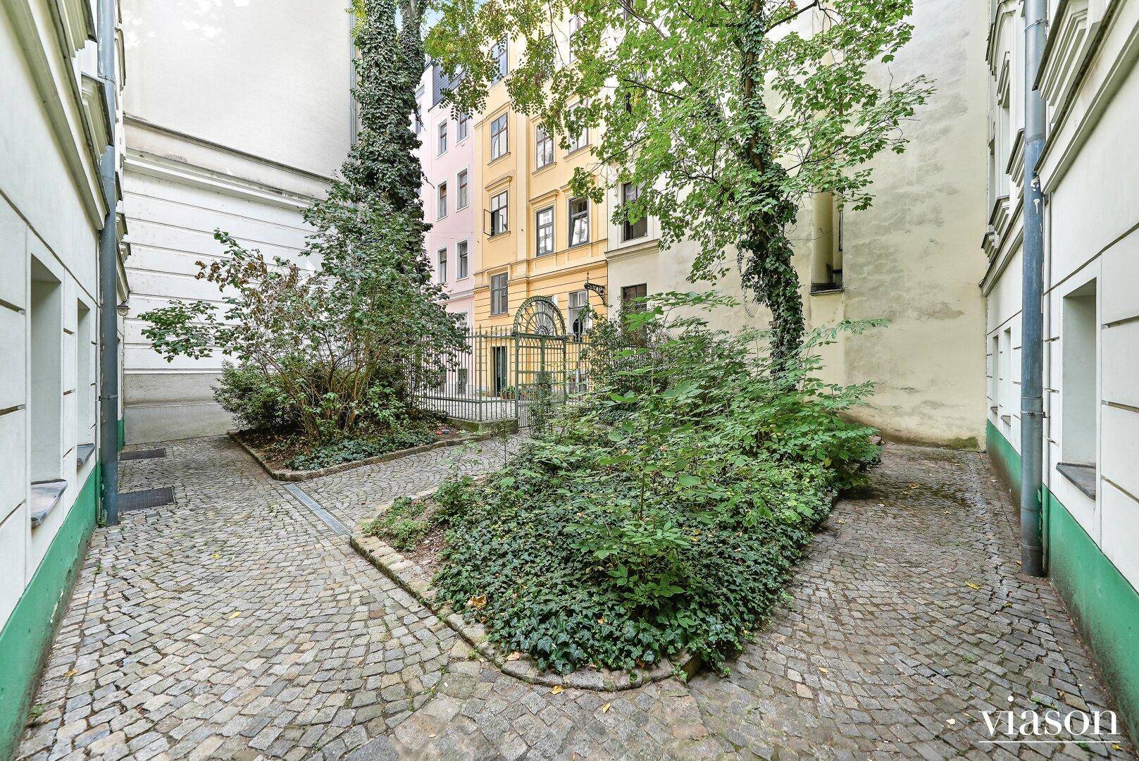 Begrünter Innenhof mit verschlungenen Wegen aus Kopfsteinpflaster zwischen historischen Gebäuden.