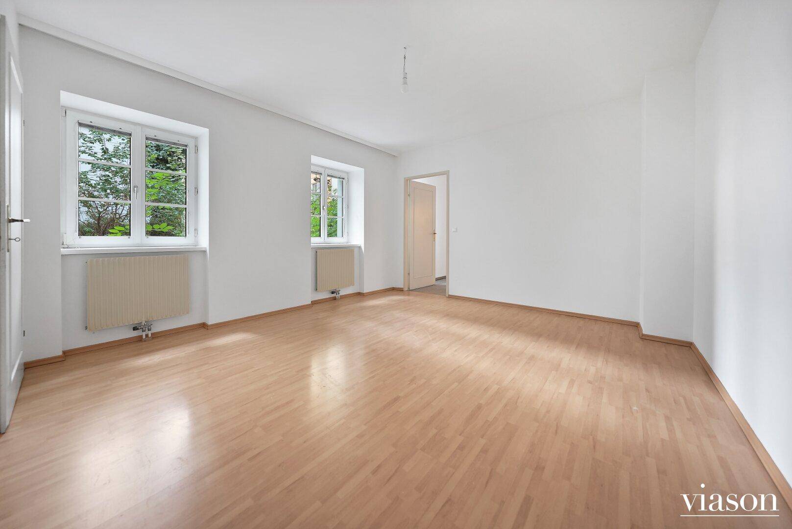 Geräumiges, helles Zimmer mit Parkettboden und zwei Fenstern, ideal für Wohn- oder Schlafbereich.