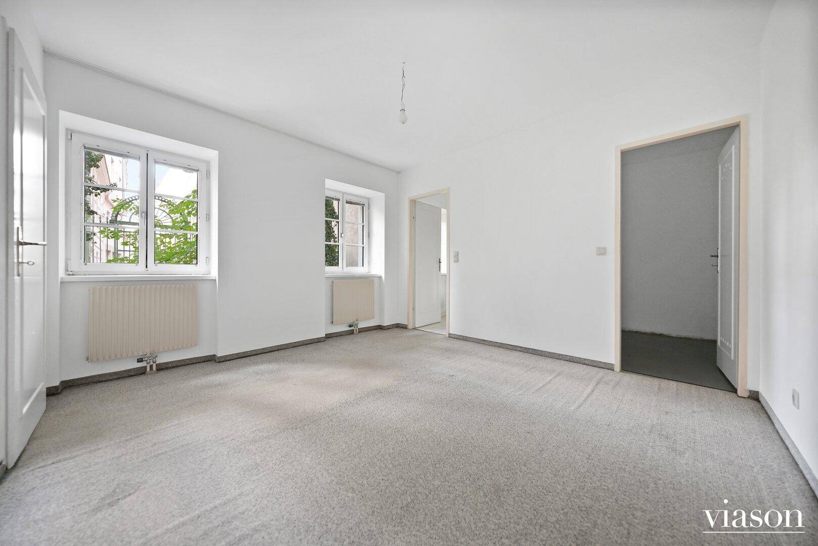 Helles Zimmer mit grauem Teppichboden und zwei Fenstern, bietet eine gemütliche Atmosphäre.