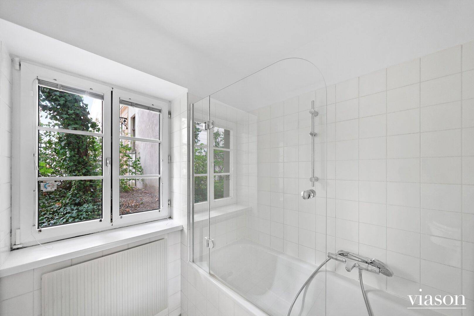 Badewanne mit Duschfunktion und Fenster, das für natürliches Licht im Badezimmer sorgt.