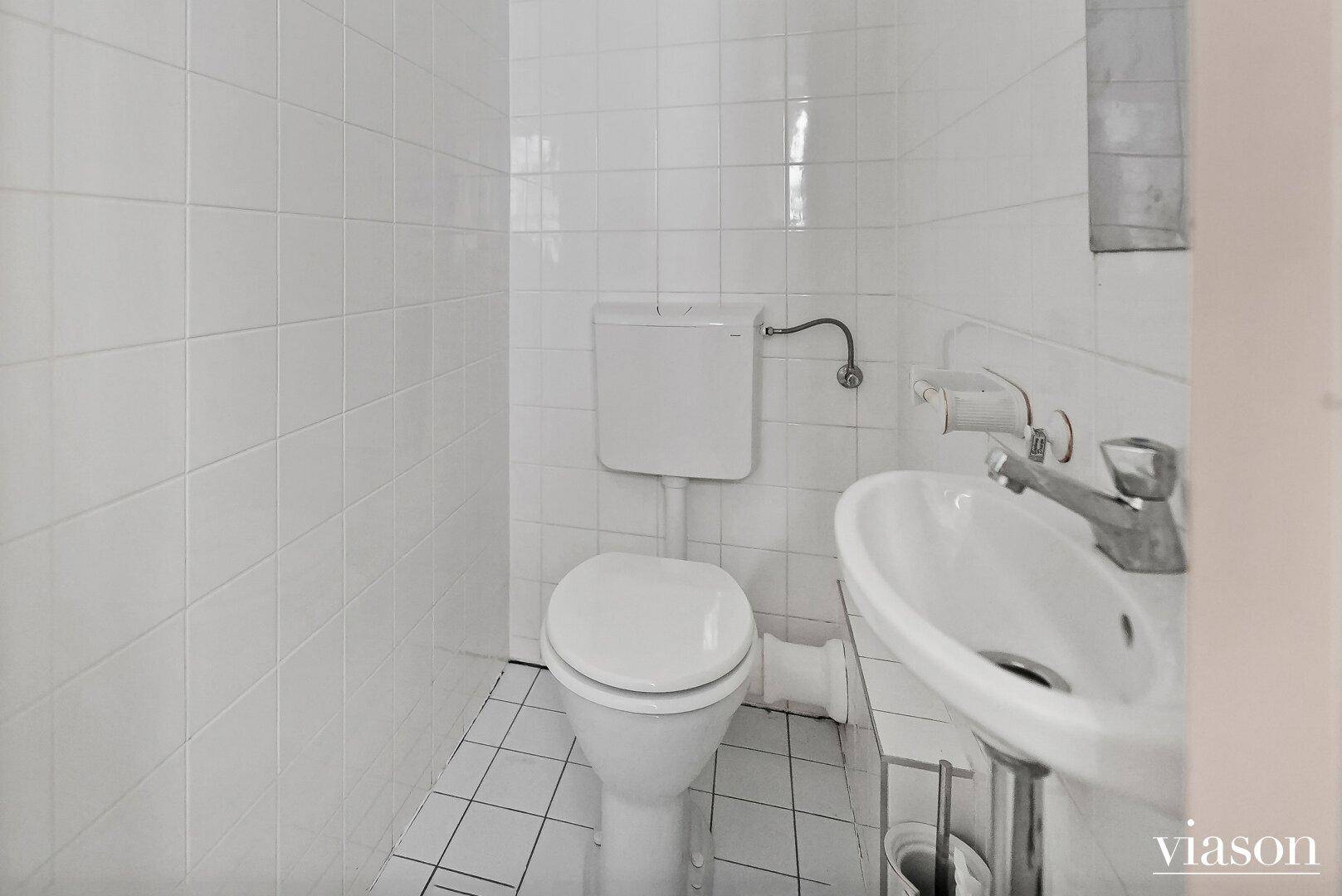 Kleines Gäste-WC mit Toilette und Waschbecken, komplett gefliest in Weiß.
