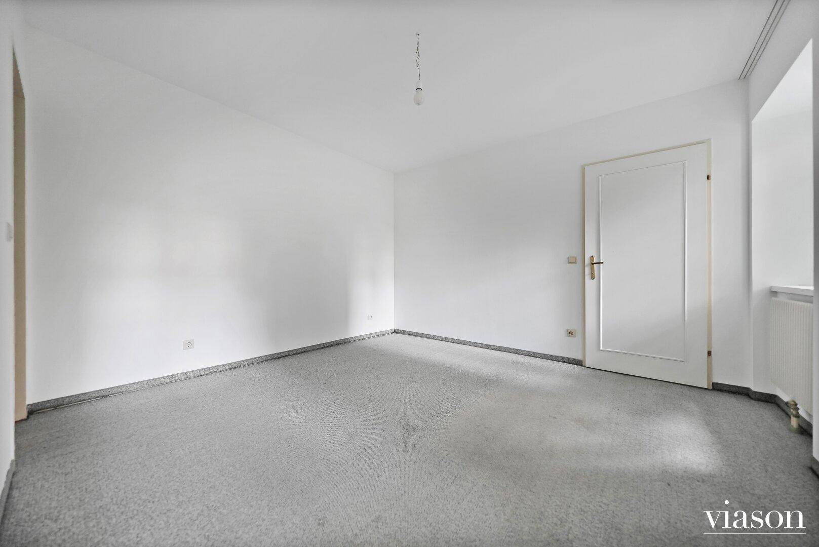 Geräumiges Zimmer mit grauem Teppichboden und weiß gestrichenen Wänden, bereit zur Einrichtung.