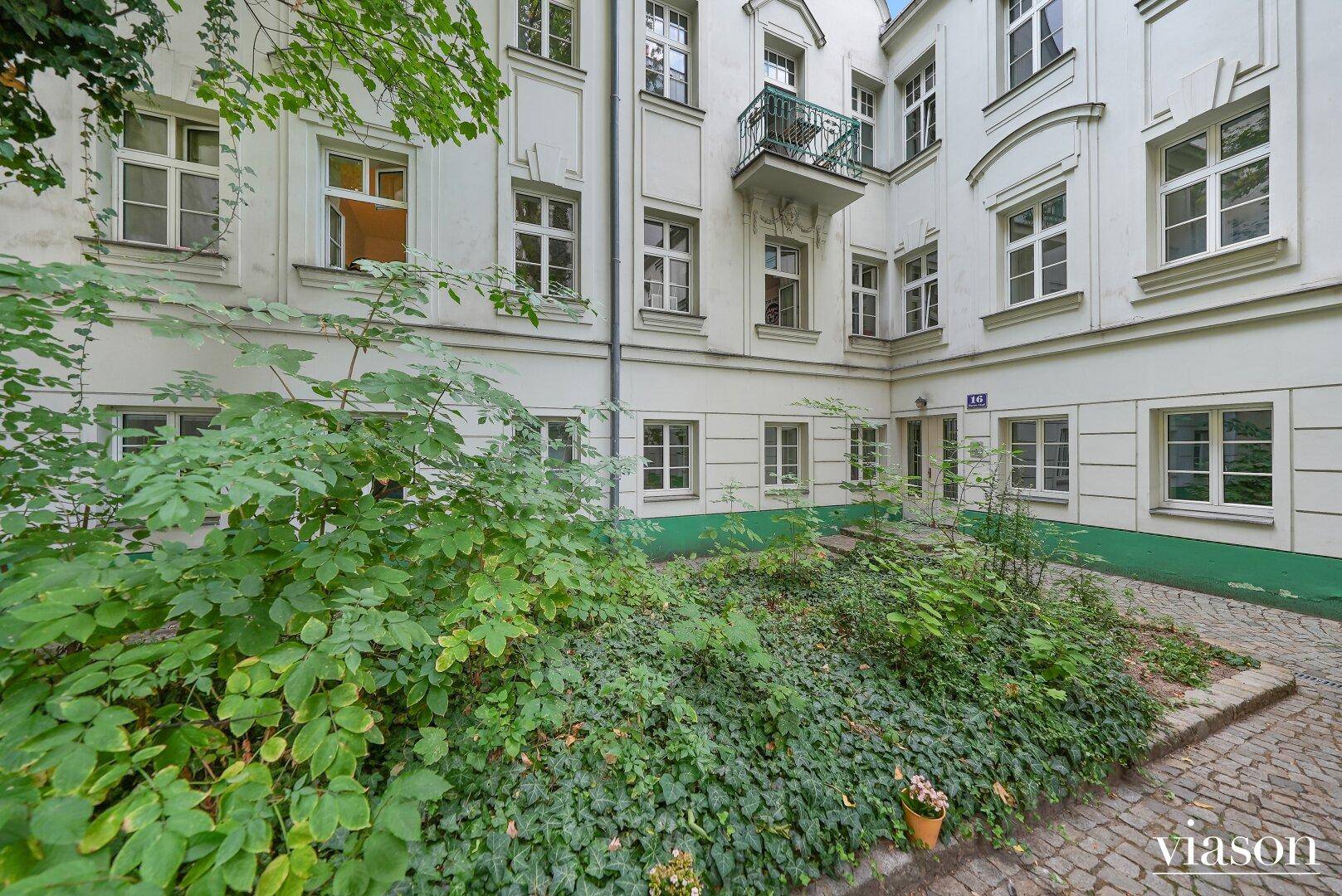 Begrünter Innenhof mit historischer Gebäudefassade und einem kleinen Balkon im Obergeschoss.