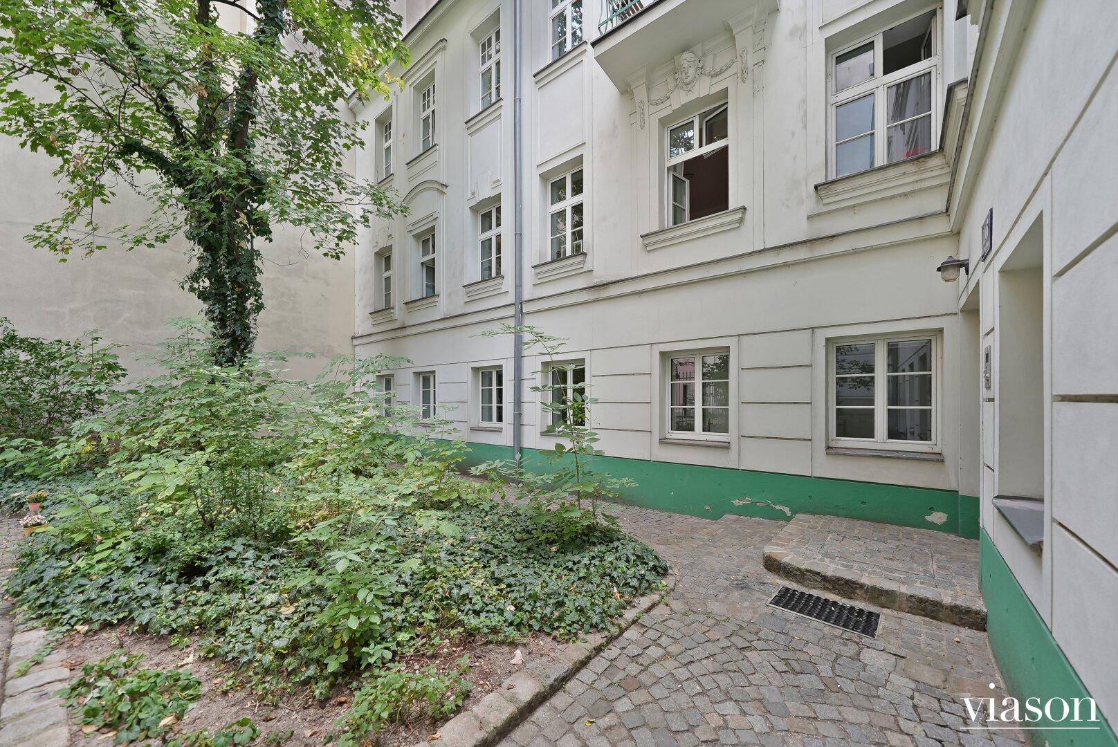 Ruhiger Innenhof mit üppiger Bepflanzung und traditionellem Kopfsteinpflaster, umgeben von Gebäuden.
