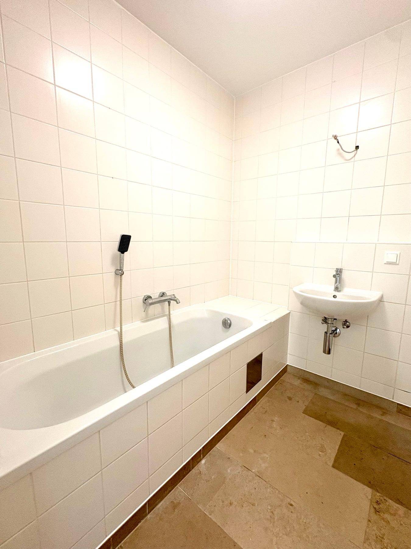 Badezimmer mit weiß gefliesten Wänden, Badewanne und kleinem Waschbecken.