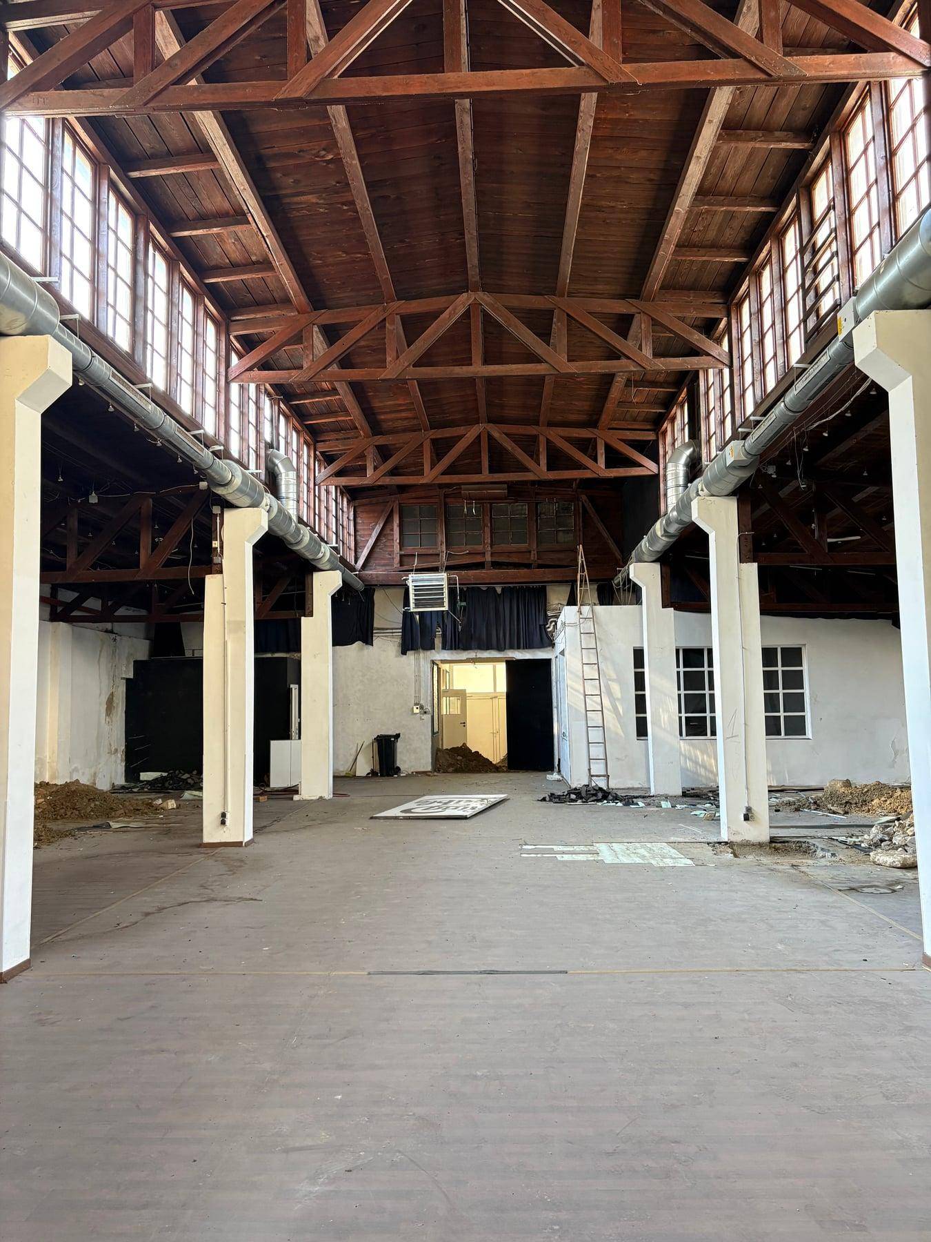 Weitere Ansicht der großen Industriehalle mit hohen Holzbalkendecken, vielen Fenstern und einer Leiter.