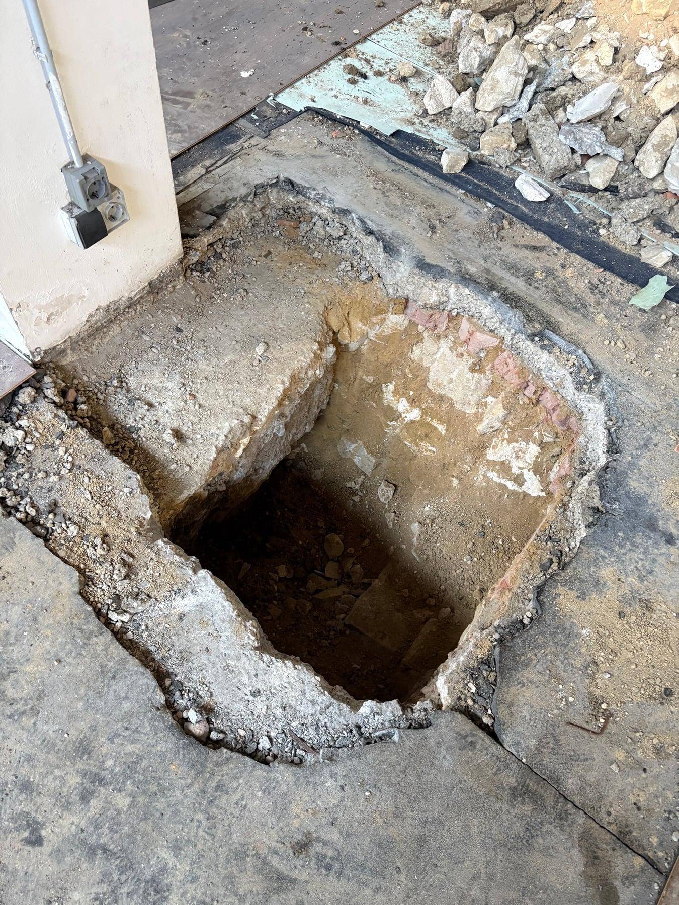 Nahaufnahme eines weiteren großen, tiefen Lochs in einem Betonboden, umgeben von Bauschutt.