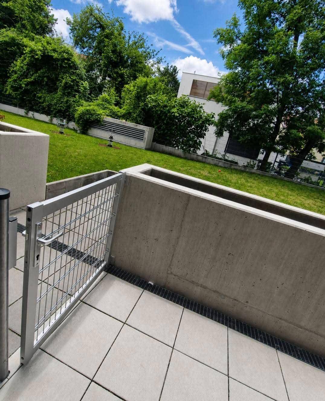 Blick von der Terrasse auf eine gepflegte Grünfläche mit Bäumen und umliegenden Gebäuden.