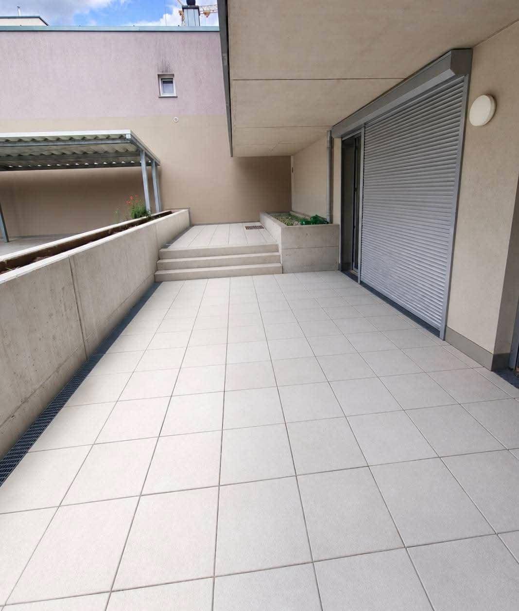 Helle, moderne Terrasse mit großen Fliesen und Rollläden, ideal für Entspannung im Freien.