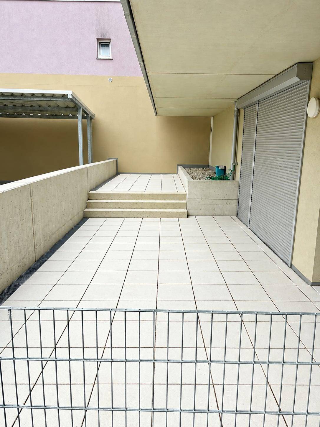 Weitläufige geflieste Terrasse mit moderner Architektur und Rollläden an den Fenstern.