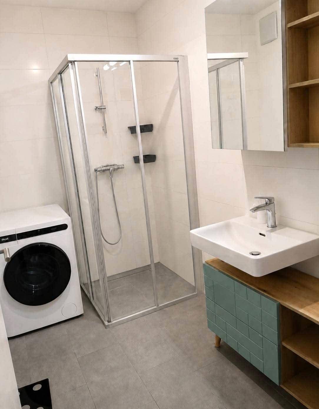 Modernes Badezimmer mit Duschkabine, Waschbecken und Waschmaschine, hell gefliest.