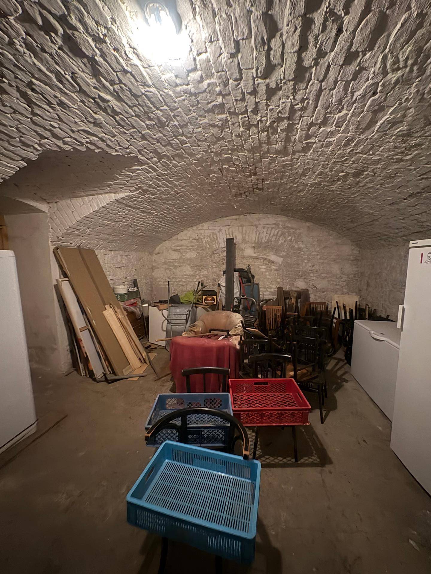 Kellerraum mit gewölbter Decke, der als Lager für Möbel und Kühlgeräte dient.