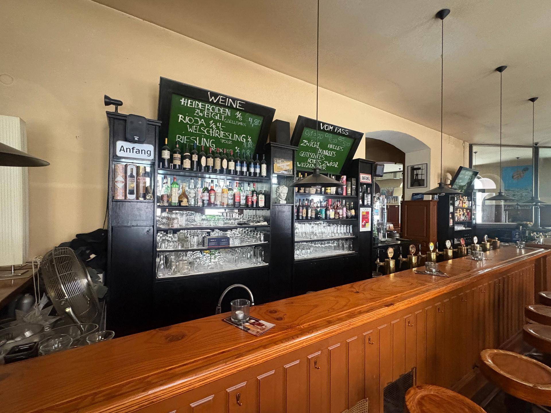 Gut ausgestattete Bar mit Holztheke, vielen Flaschen und Gläsern, bereit für den Gastronomiebetrieb.