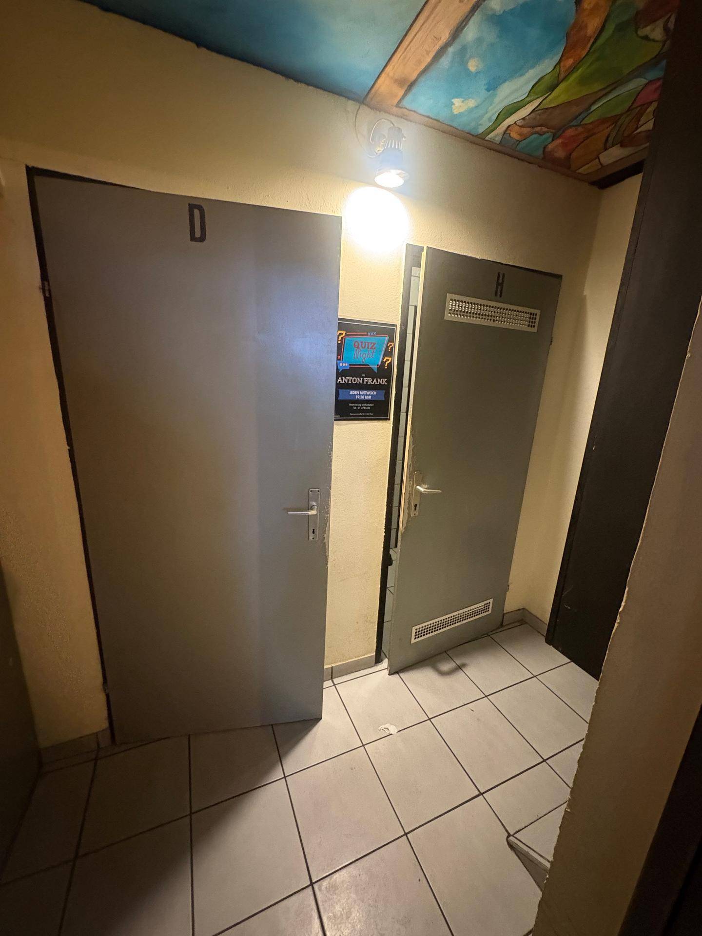 Flur, der zu den Toiletten führt, mit grauen Türen und Fliesenboden in einem Gewerbeobjekt.
