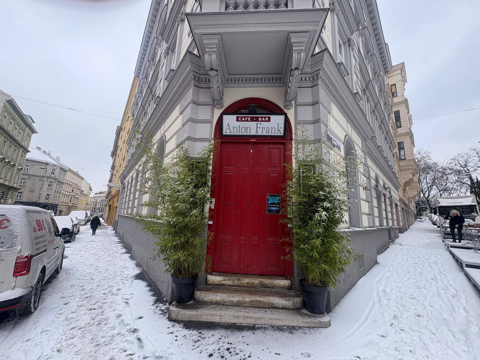 Vorderansicht des Eingangs eines Eckgebäudes mit roter Tür und Bambuspflanzen im Schnee.