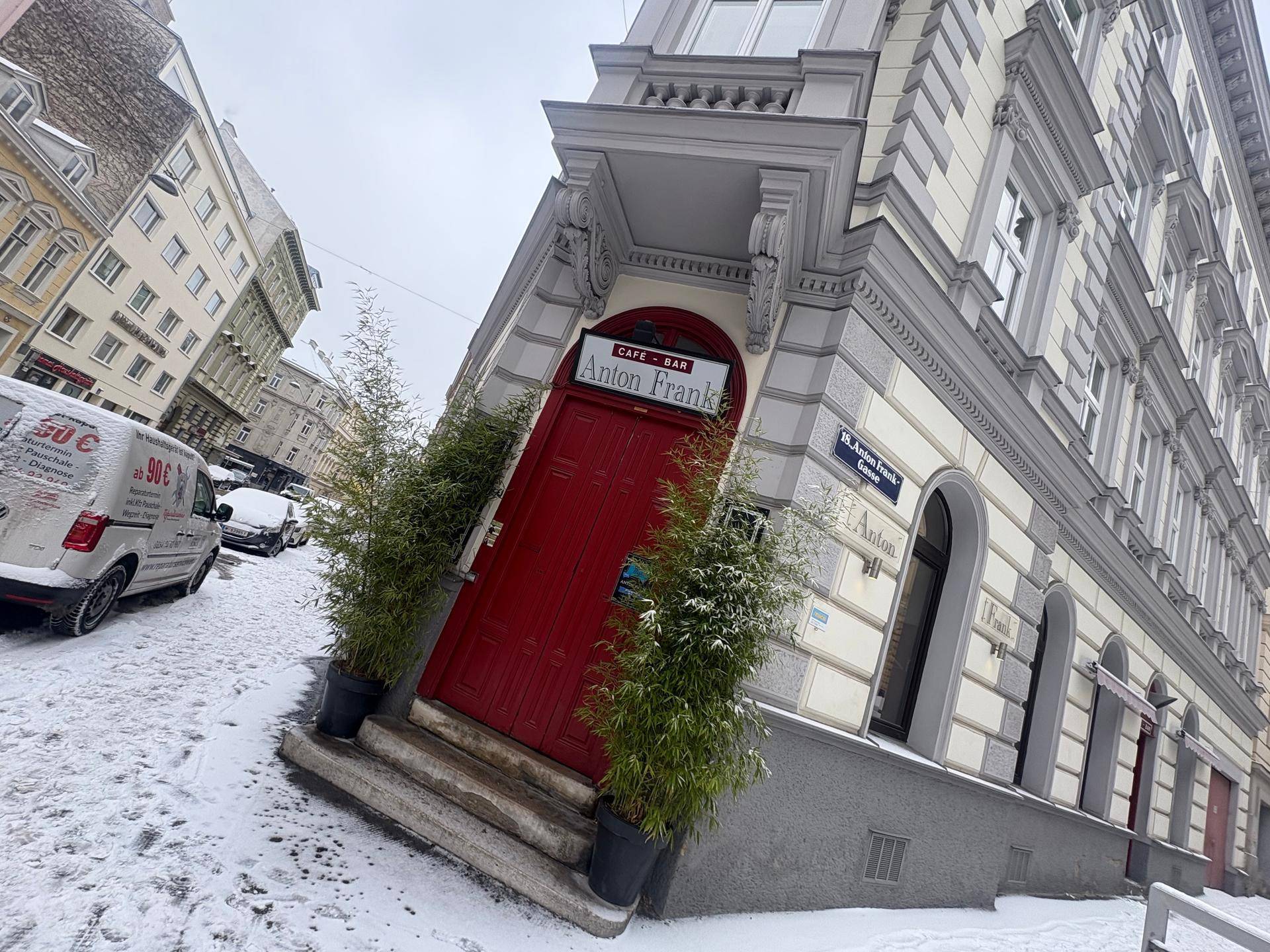 Eingang eines Eckgebäudes mit roter Tür und Bambuspflanzen, umgeben von Schnee.
