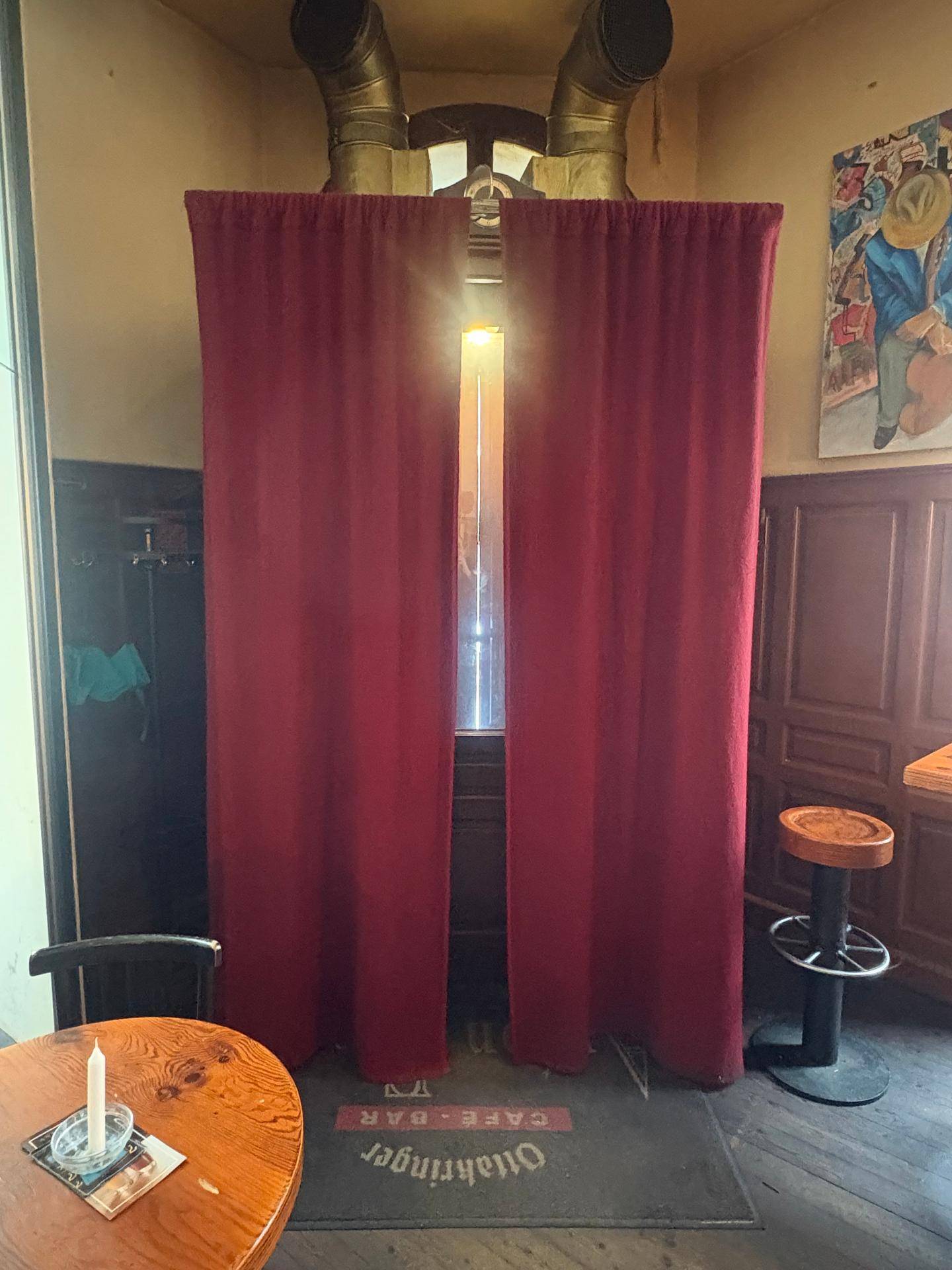 Rote Vorhänge vor einem hohen Fenster in der Bar, das Tageslicht hereinlässt.