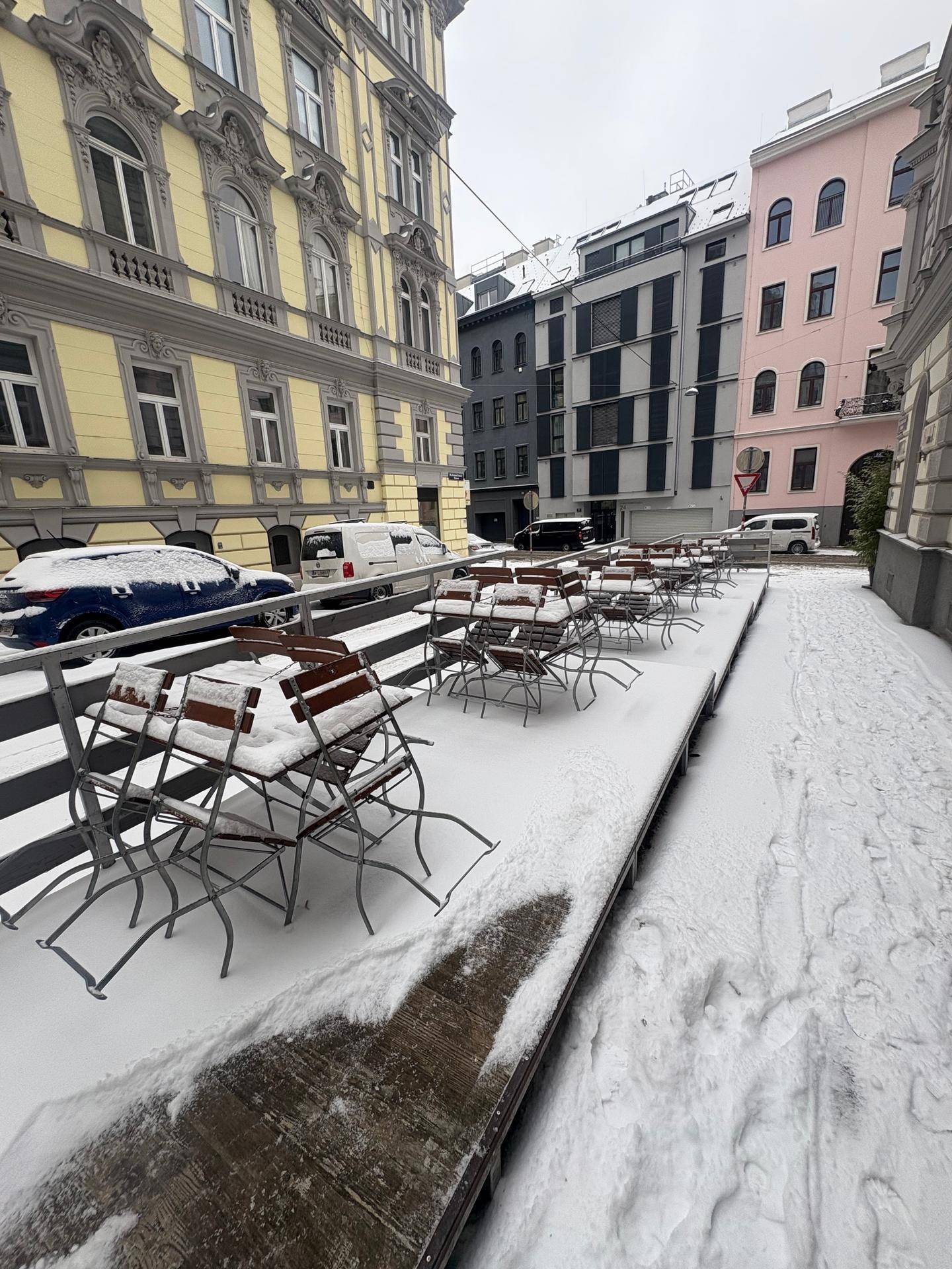 Verschneite Außenterrasse mit Tischen und Stühlen vor einem Gebäude in der Stadt.