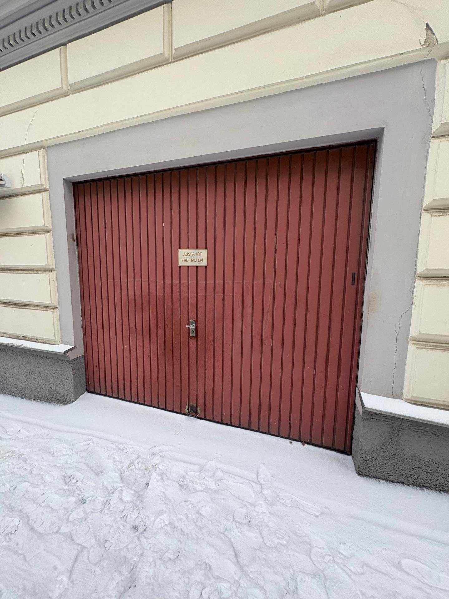 Rotes Garagentor an einem Gebäude, umgeben von Schnee auf dem Boden.