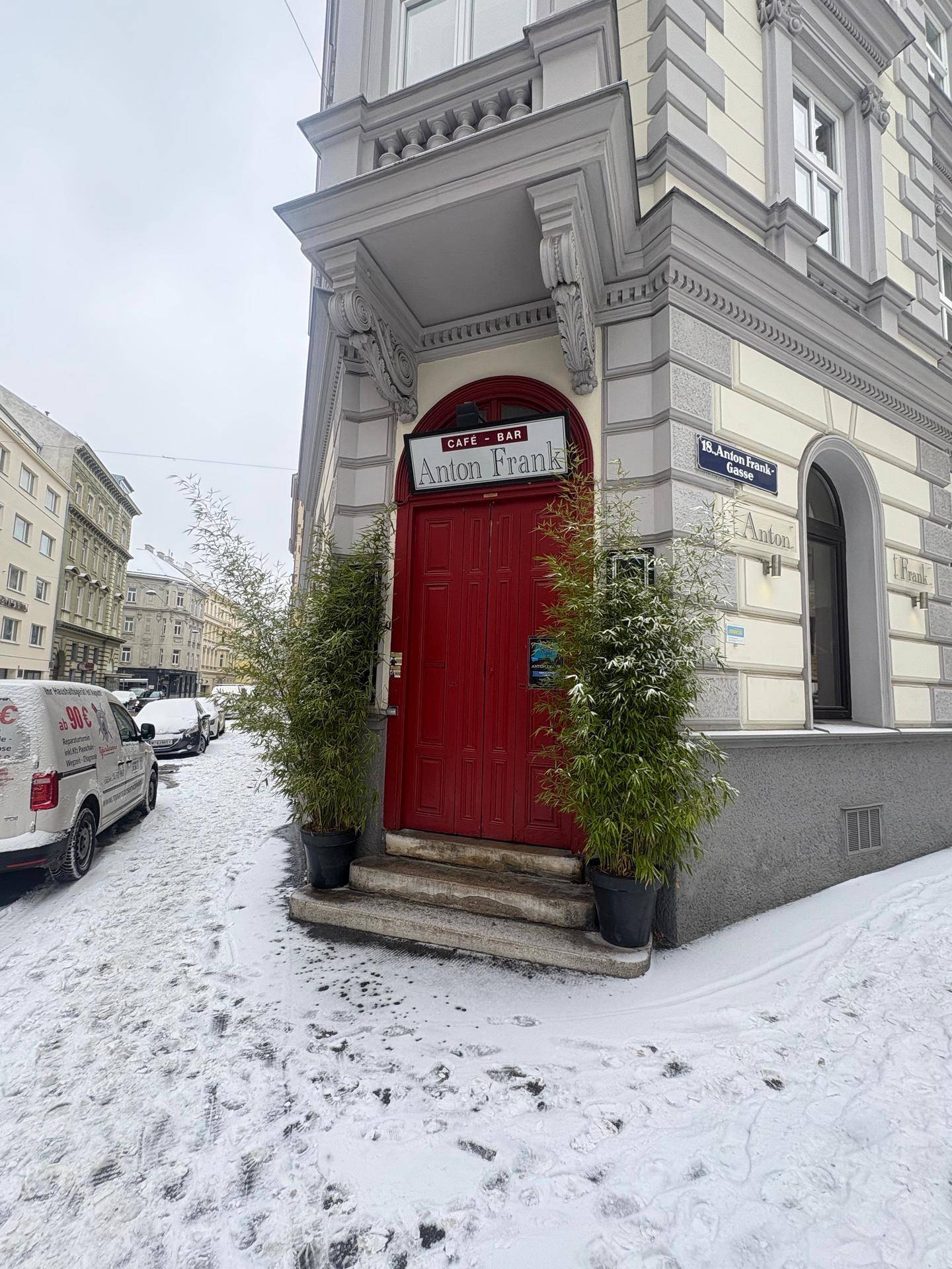 Eingang eines Eckgebäudes mit roter Tür und Bambuspflanzen, umgeben von Schnee.