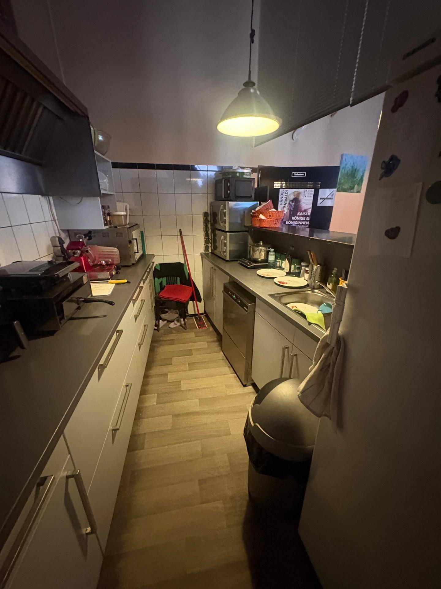 Kleine, funktionale Gewerbeküche mit Spülbereich, Arbeitsflächen und Lagerregalen.