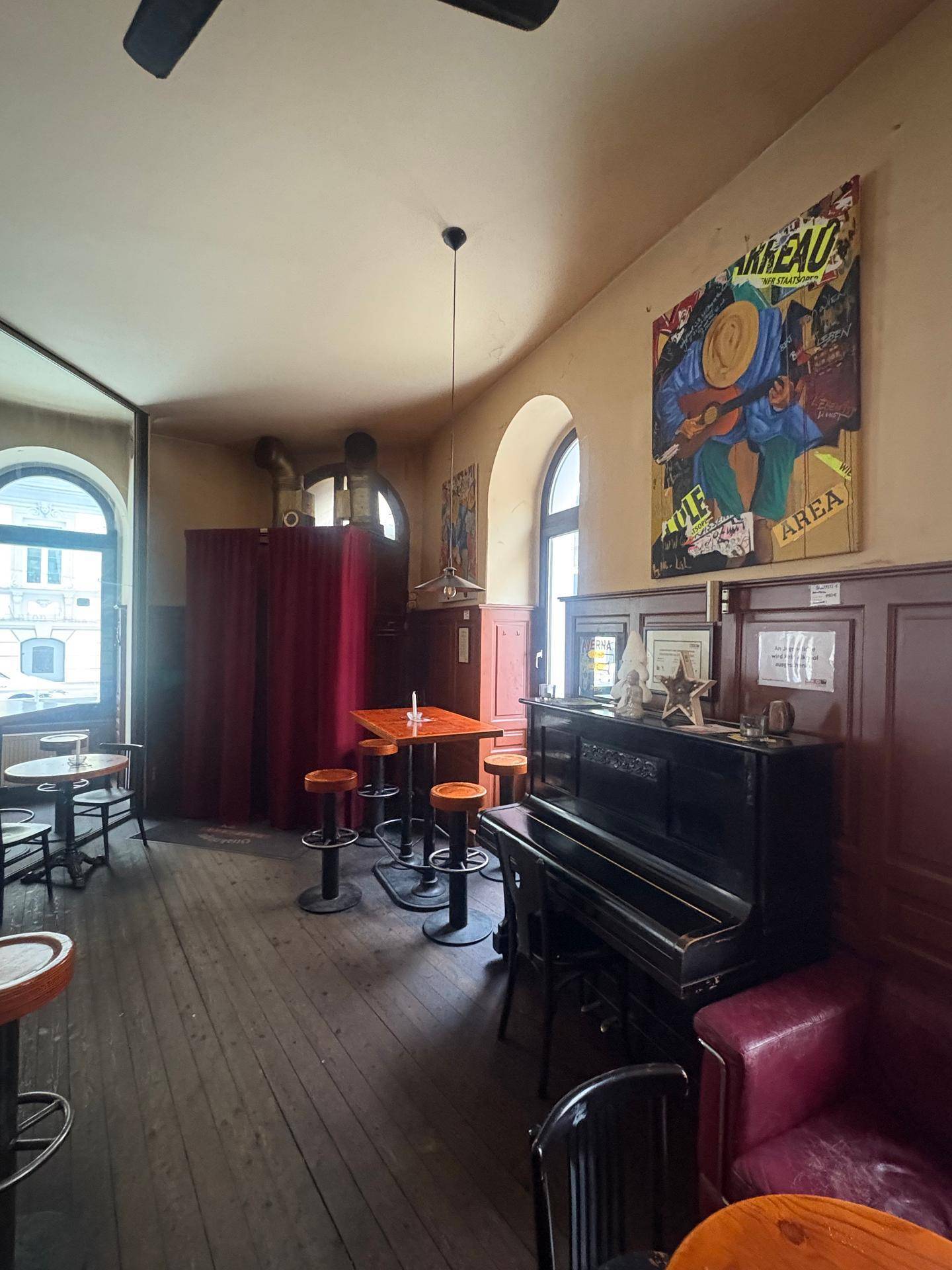 Barbereich mit einem Klavier, Holzboden, roten Vorhängen und Kunstwerken an den Wänden.