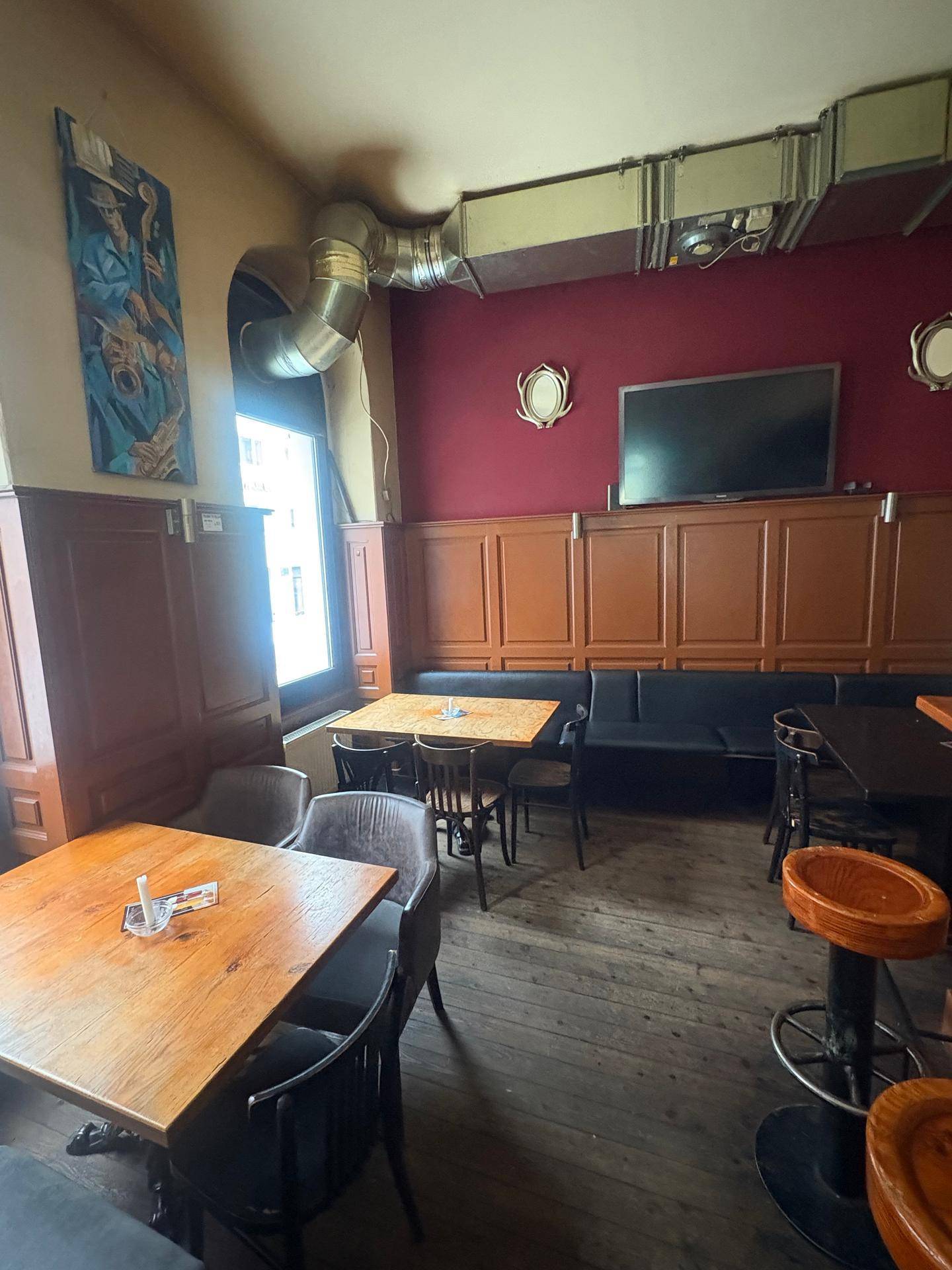 Gemütlicher Sitzbereich in der Bar mit Holztischen, Bänken und einer roten Akzentwand.