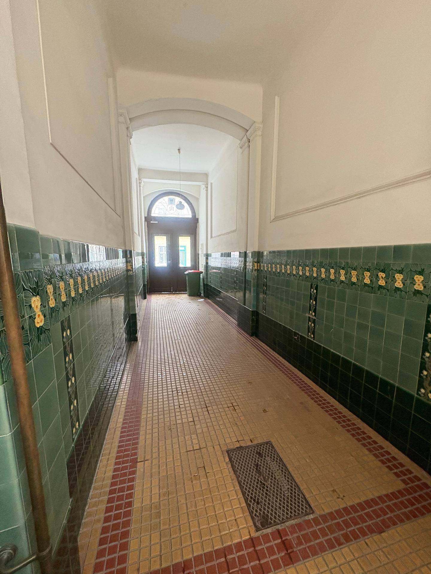 Langer Flur mit dekorativen grünen Fliesen an den Wänden und gemustertem Boden in einem Altbau.