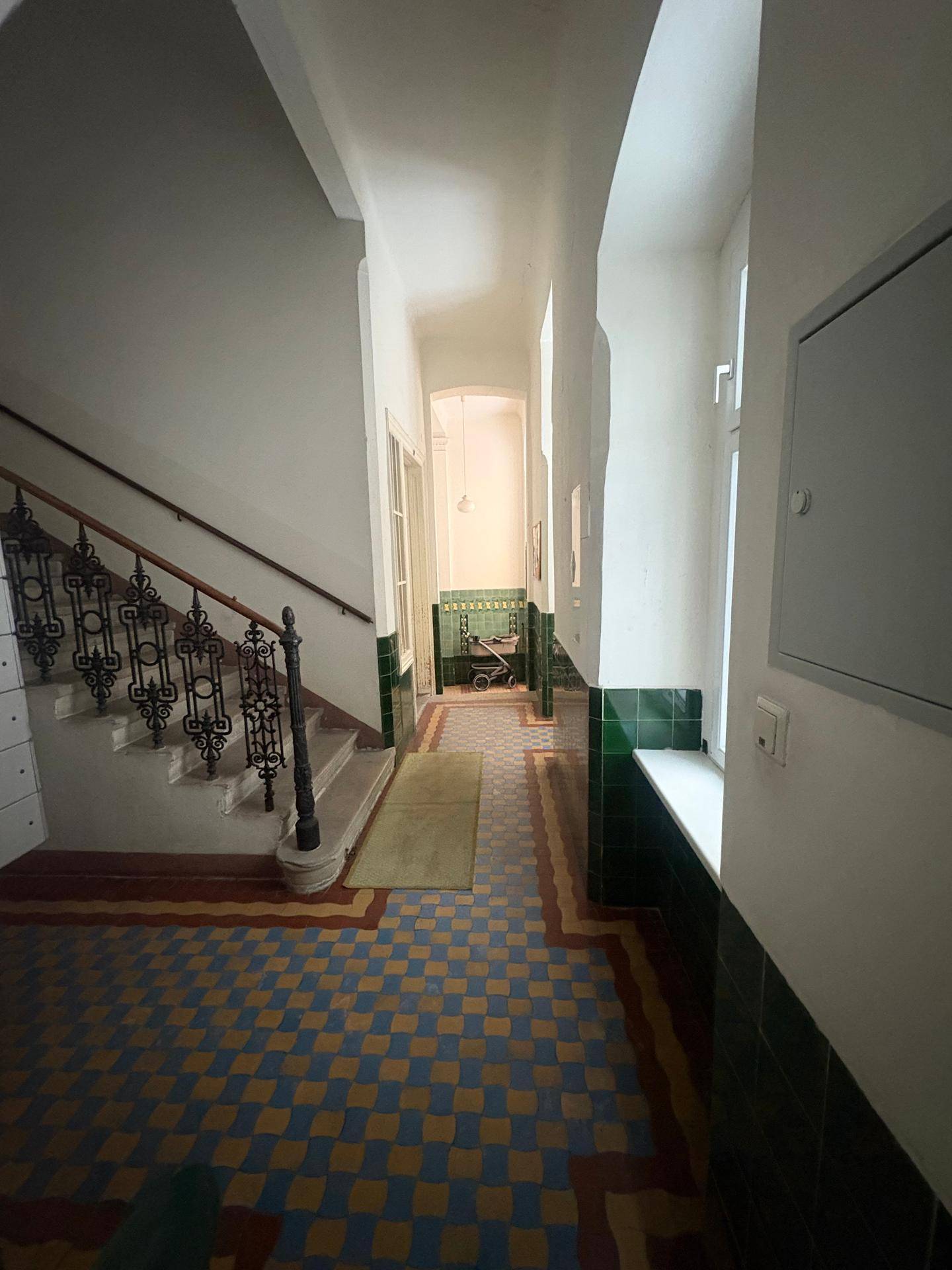 Historisches Treppenhaus mit kunstvollem Geländer und farbigen Fliesenböden in einem Altbau.