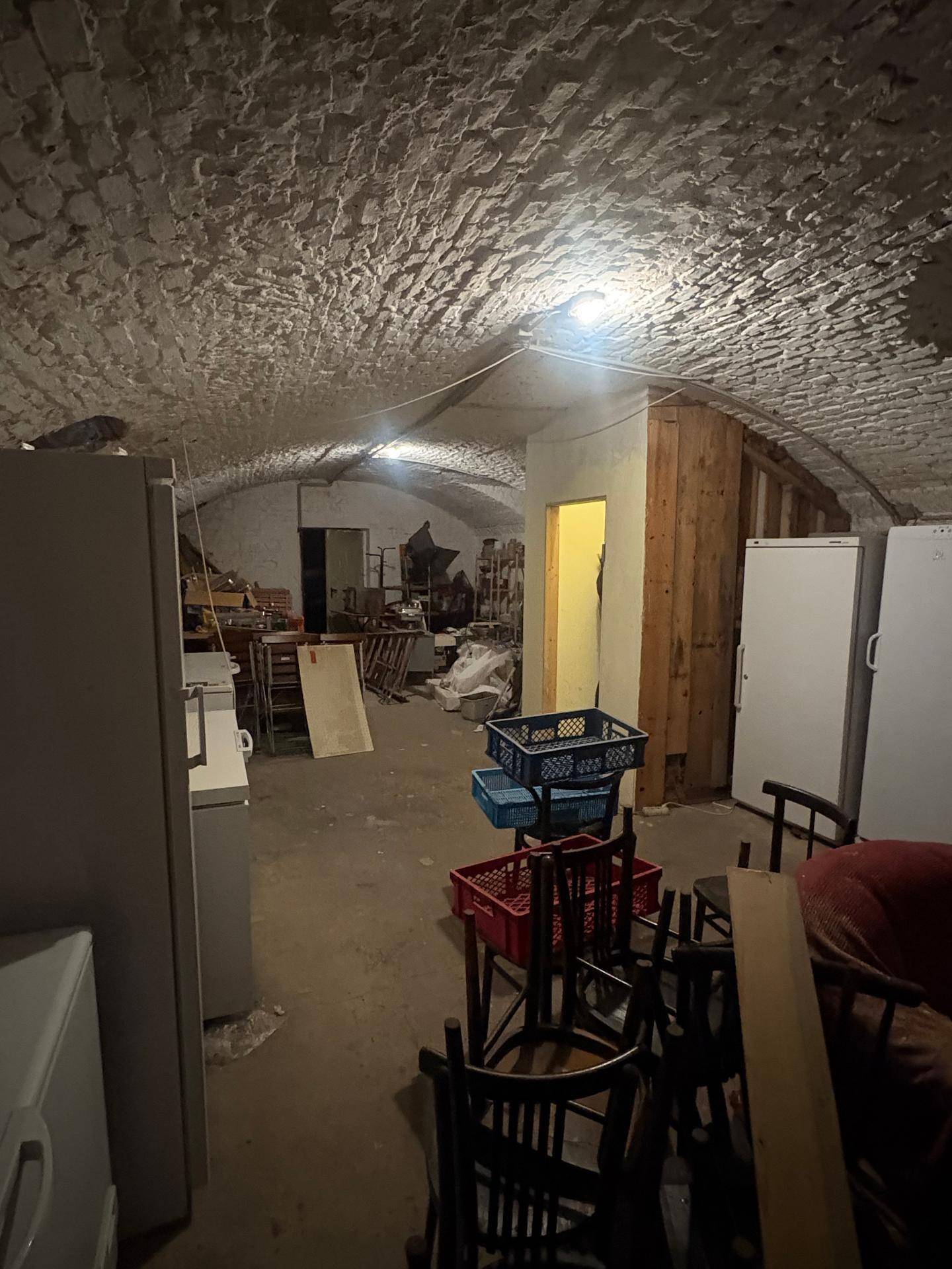 Kellerraum mit gewölbter Decke, der als Lager für Möbel und Kühlgeräte dient.