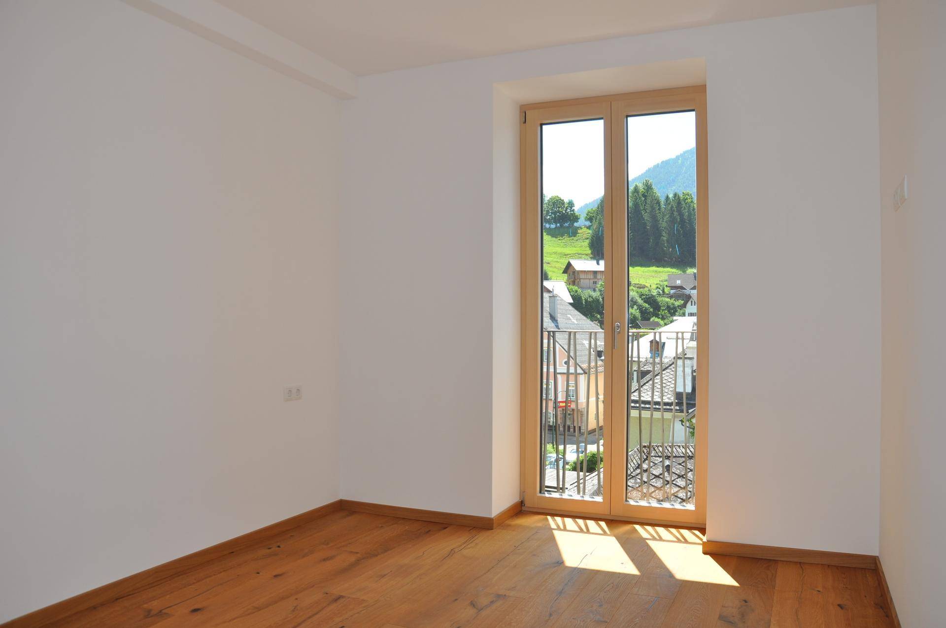 Lichtdurchflutetes Schlafzimmer mit Holzboden und französischem Balkon, der einen malerischen Bergblick ermöglicht.