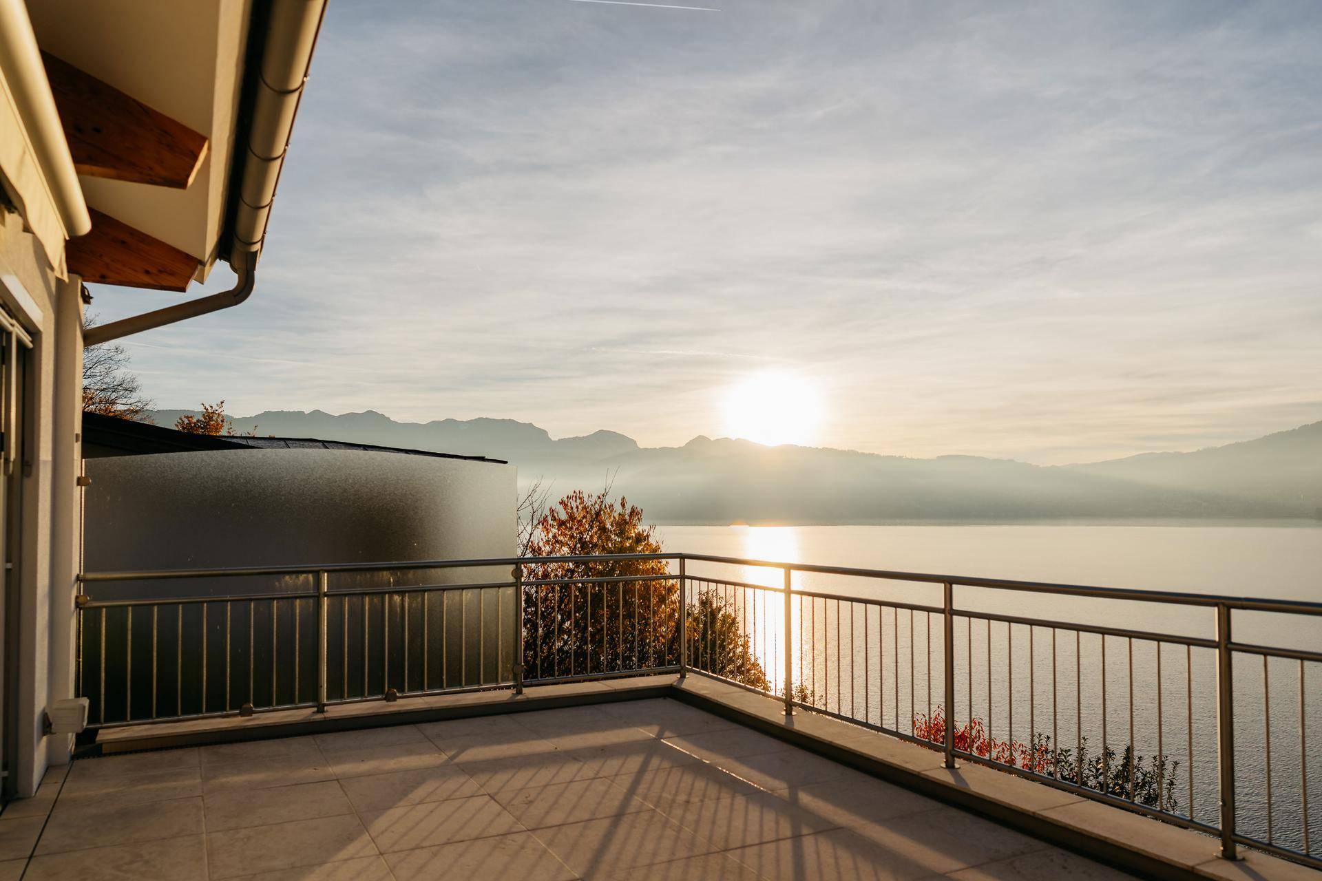 Geräumige Terrasse mit Fliesenboden und atemberaubendem Seeblick bei Sonnenaufgang.