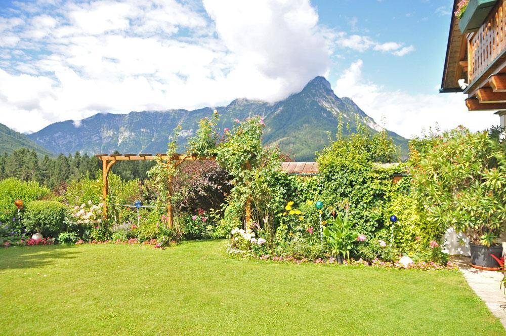 Gepflegter Garten mit blühenden Pflanzen, einer Holzpergola und einem beeindruckenden Bergblick im Hintergrund.
