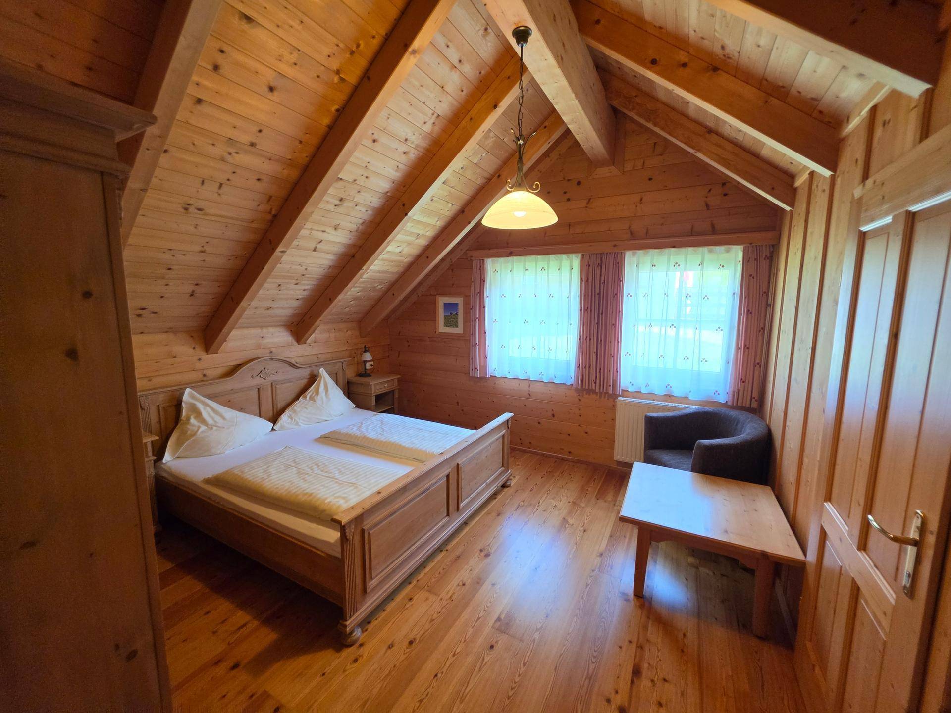 Schlafzimmer im Dachgeschoss mit Holzwänden, Holzboden, Doppelbett und schrägen Decken, hell und gemütlich.