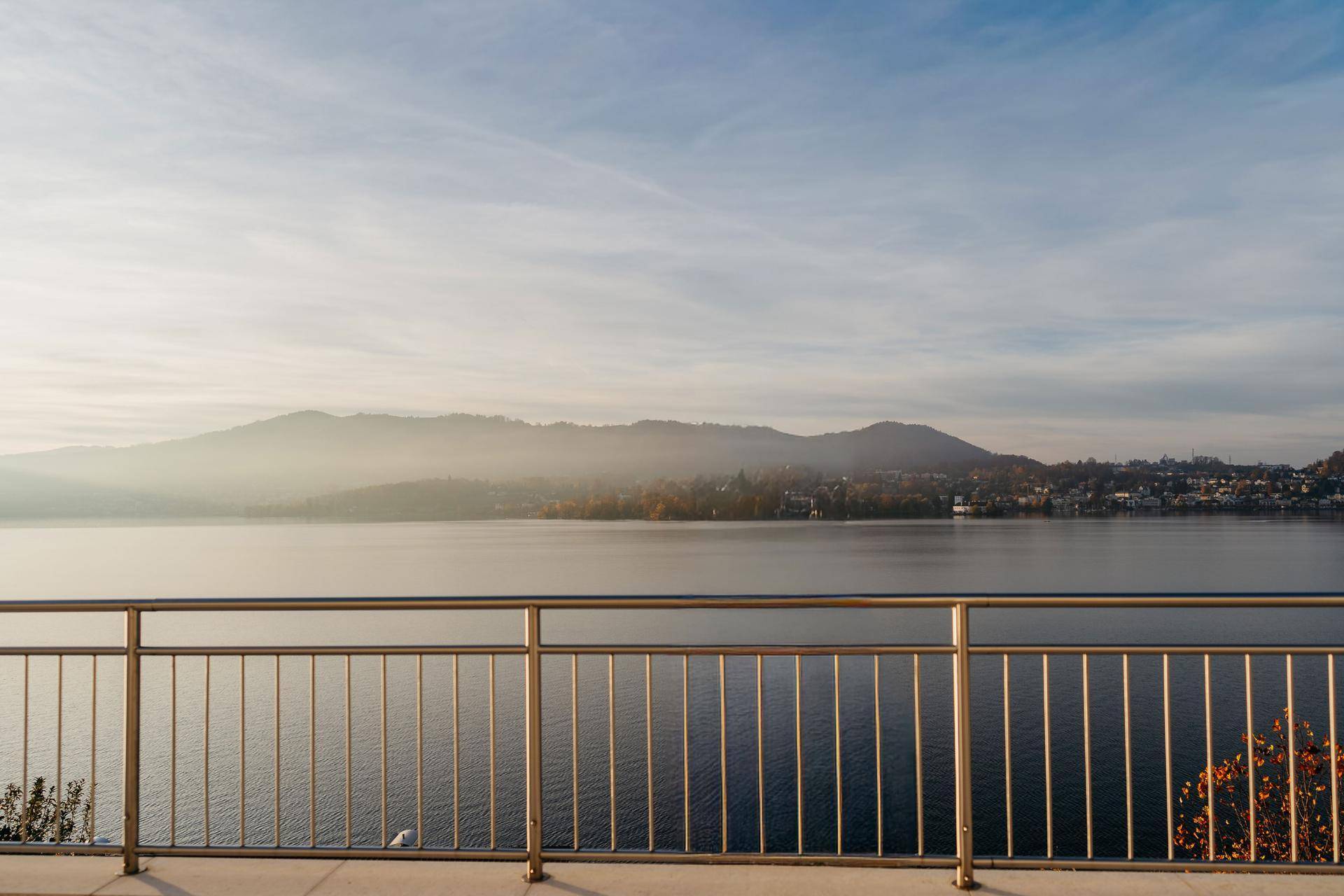 Panoramablick vom Balkon auf den See und die umliegenden Berge an einem klaren Tag.