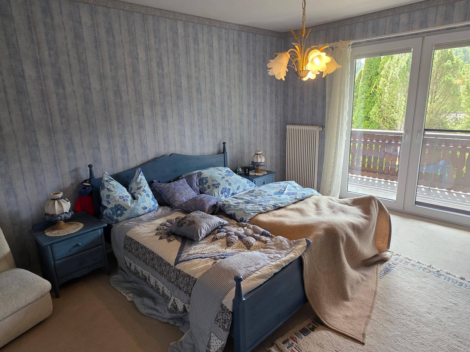 Helles Schlafzimmer mit blauem Bett, passender Tapete und Zugang zum Balkon.