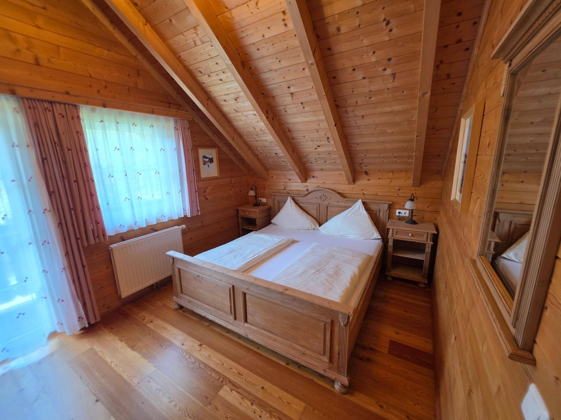 Gemütliches Schlafzimmer mit Holzboden, Holzwänden, Doppelbett und Nachttischen, gut beleuchtet durch Fenster.