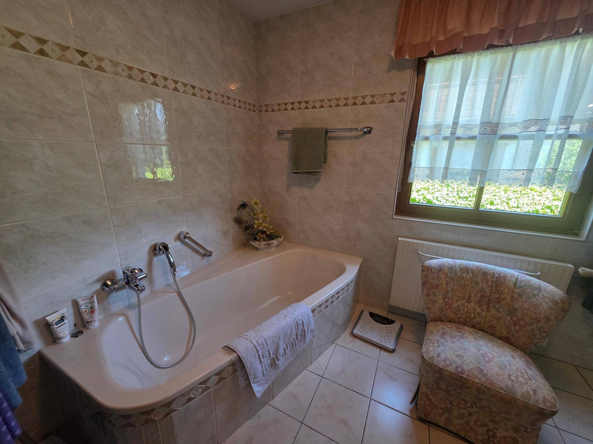 Badezimmer mit Badewanne, Fliesenboden und Fenster für natürliches Licht.