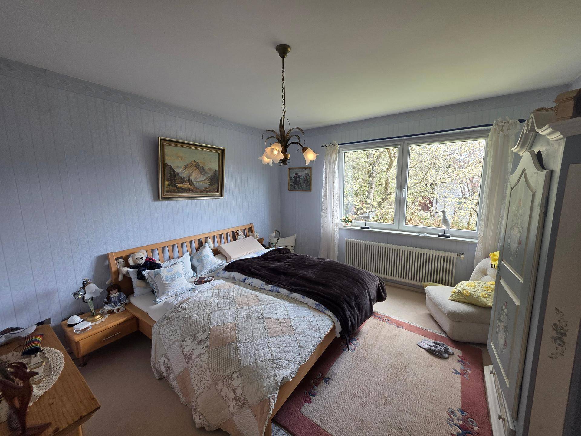 Geräumiges Schlafzimmer mit zwei Einzelbetten, blauer Tapete und Fensterblick ins Grüne.