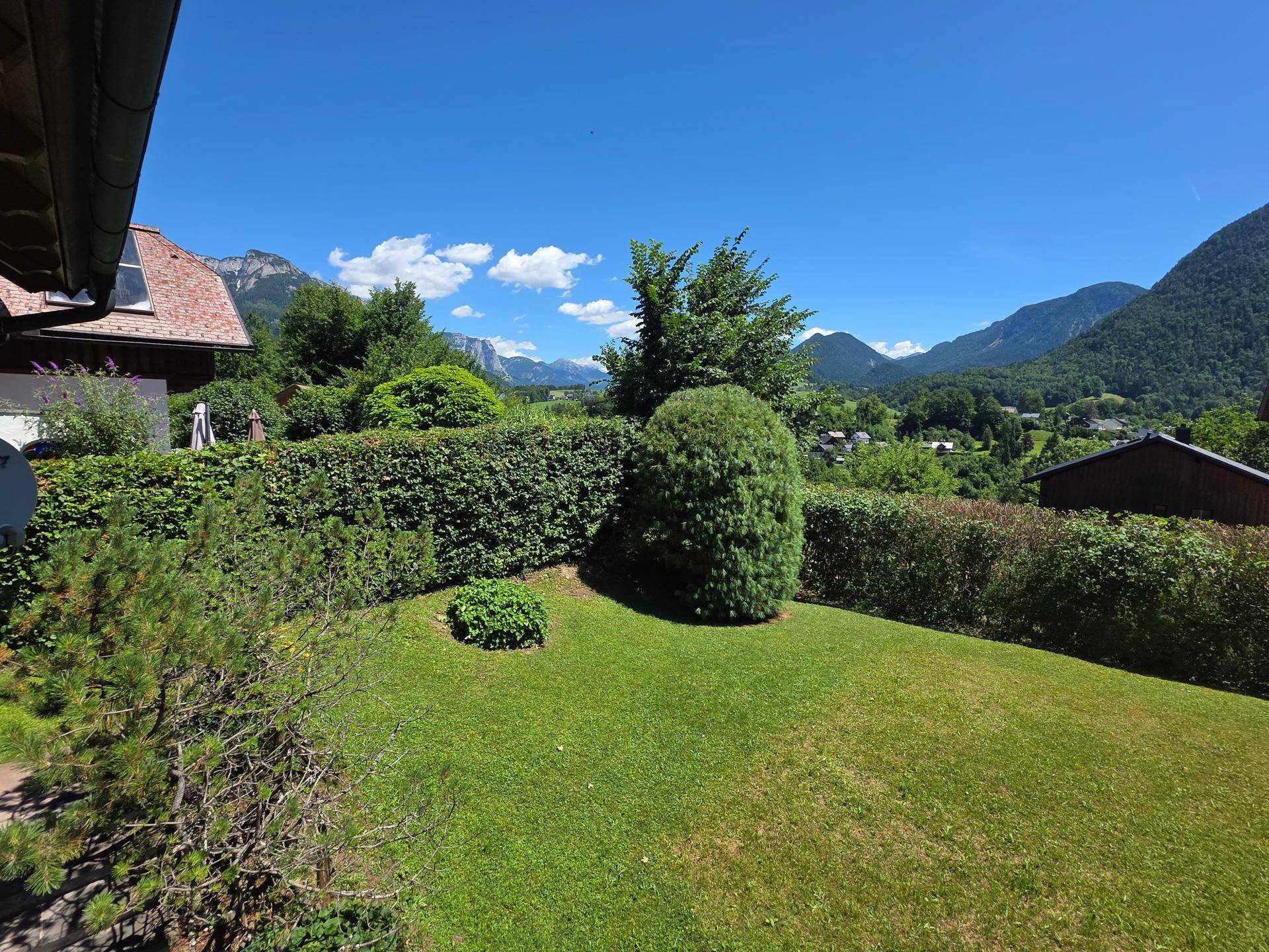 Gepflegter Gartenbereich mit Rasenfläche und Hecken, umgeben von einer malerischen Berglandschaft.