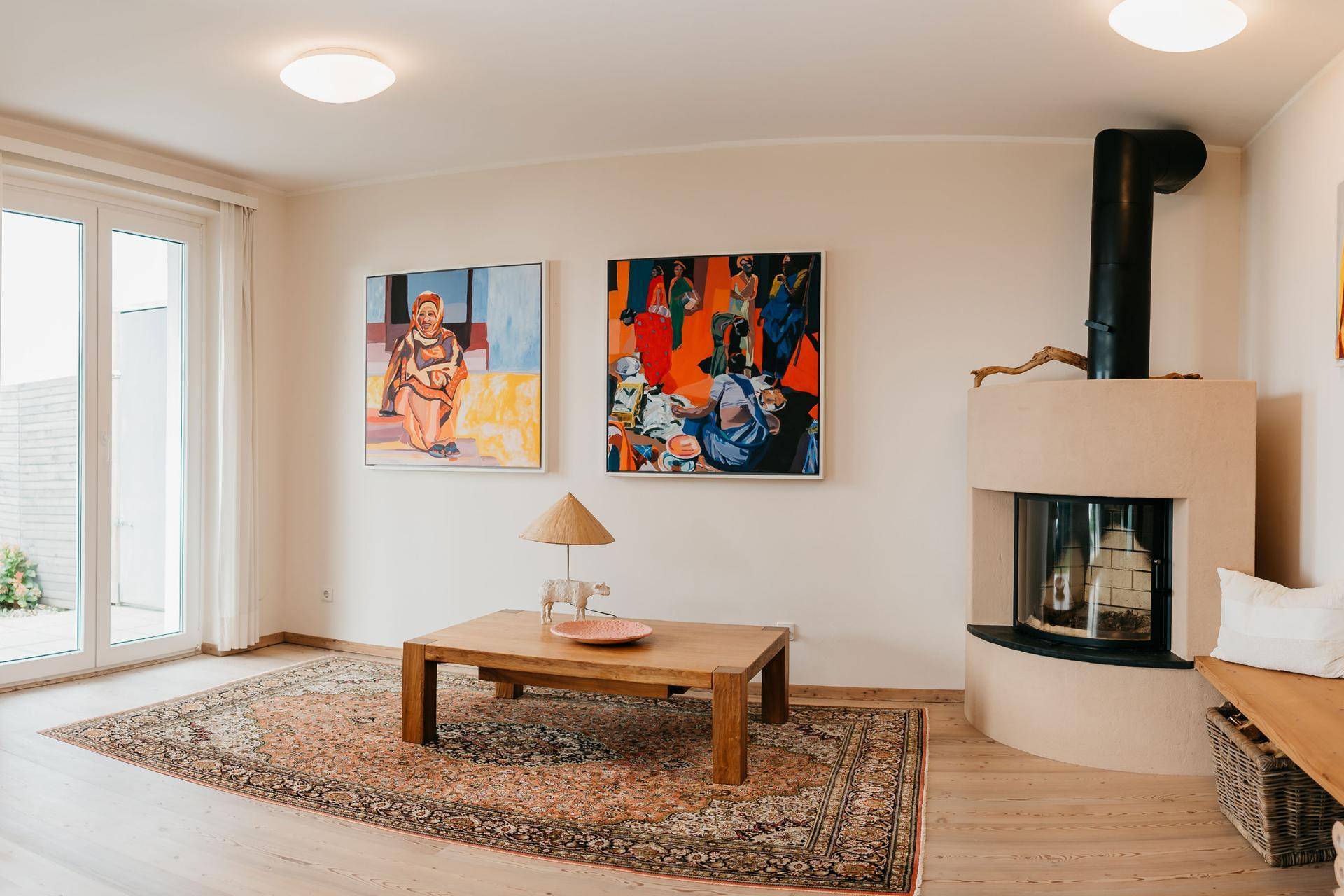 Helles Wohnzimmer mit Kamin, Holztisch und farbenfrohen Kunstwerken.