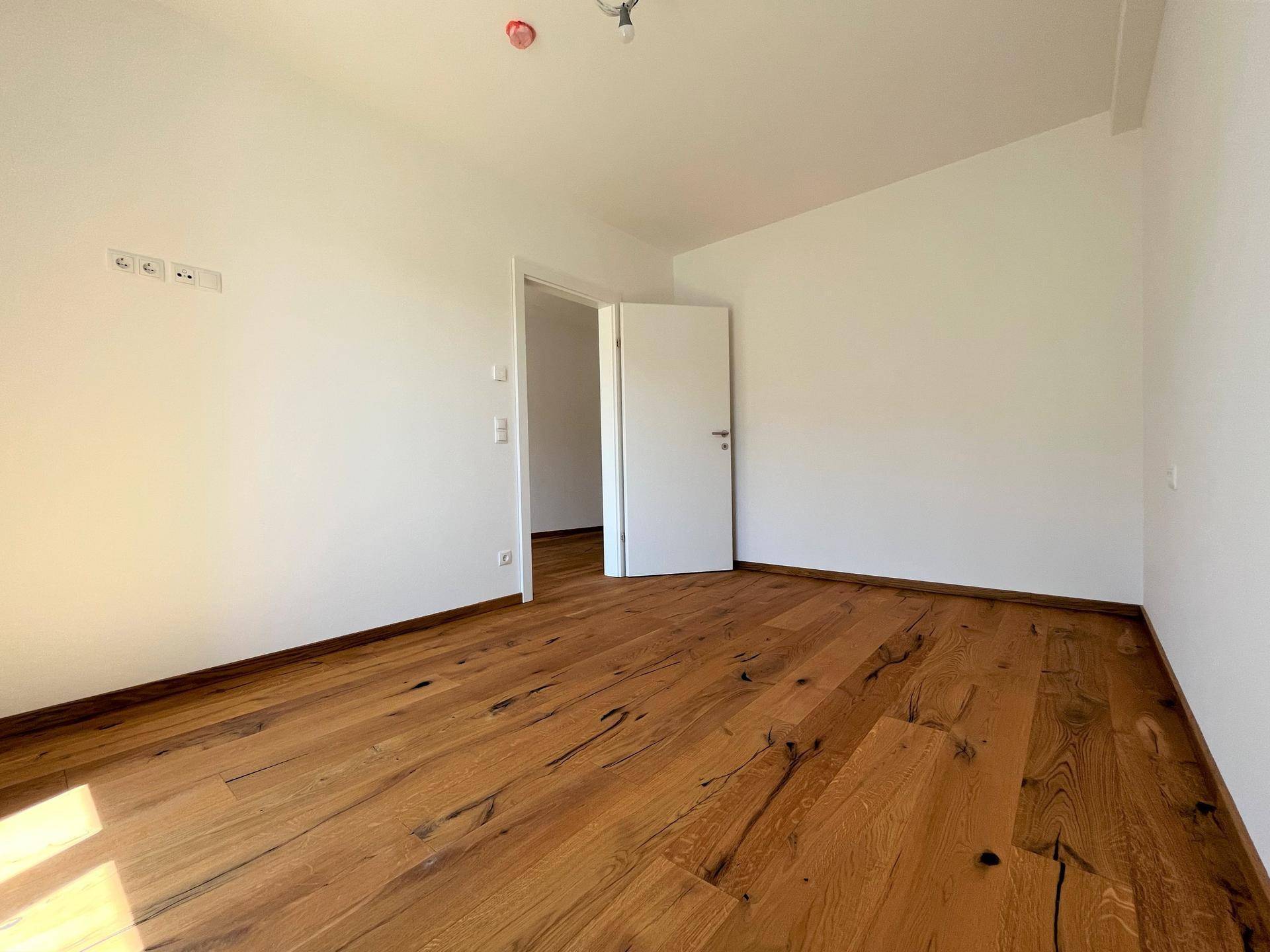Geräumiges Zimmer mit charaktervollem Holzboden und weiß gestrichenen Wänden, ideal für Schlaf- oder Arbeitsbereich.