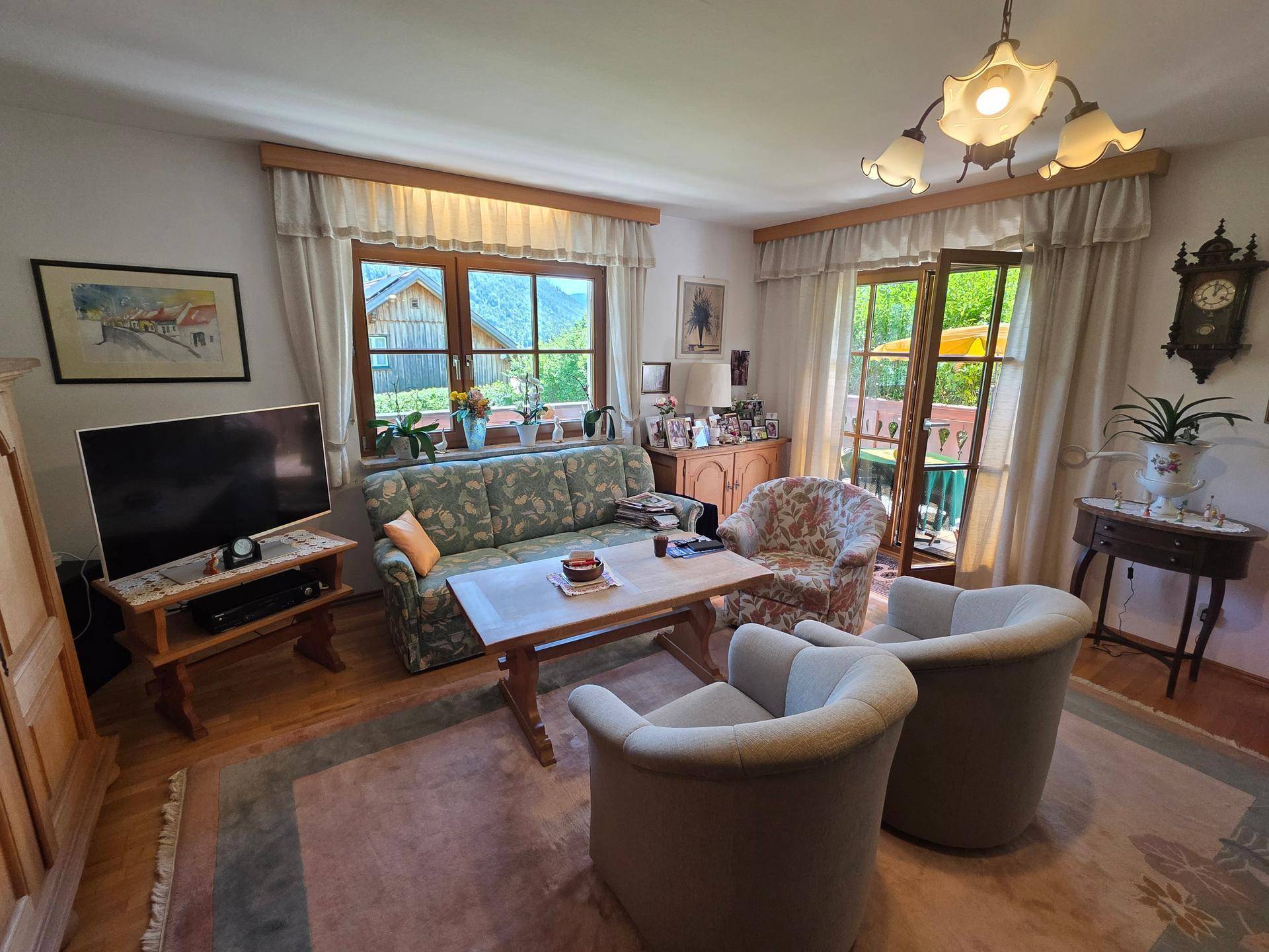 Gemütliches Wohnzimmer mit traditionellen Möbeln, Teppichboden und Zugang zu einem Balkon.