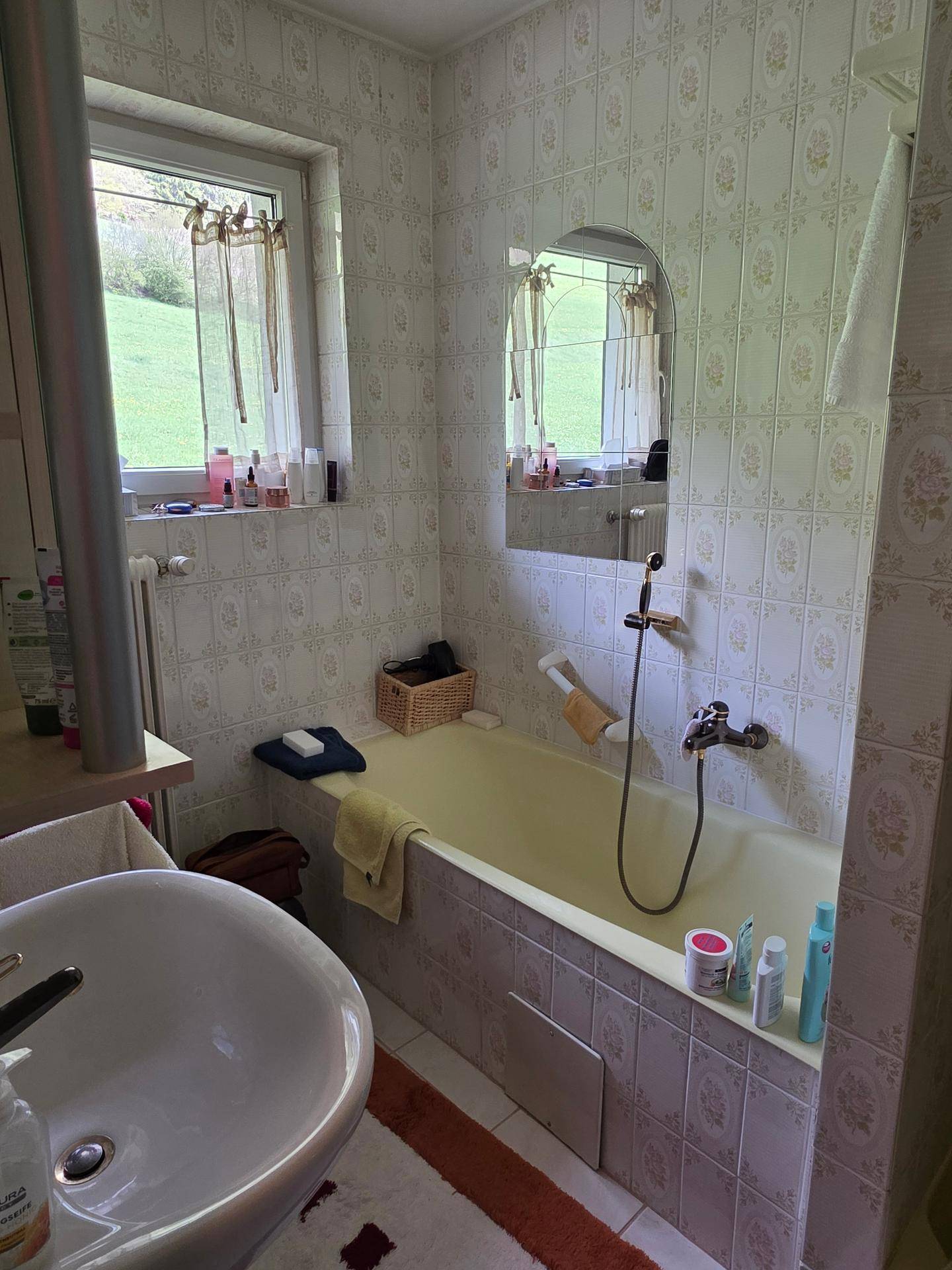 Badezimmer mit Badewanne, Waschbecken und gemusterten Fliesen, inklusive Fenster.