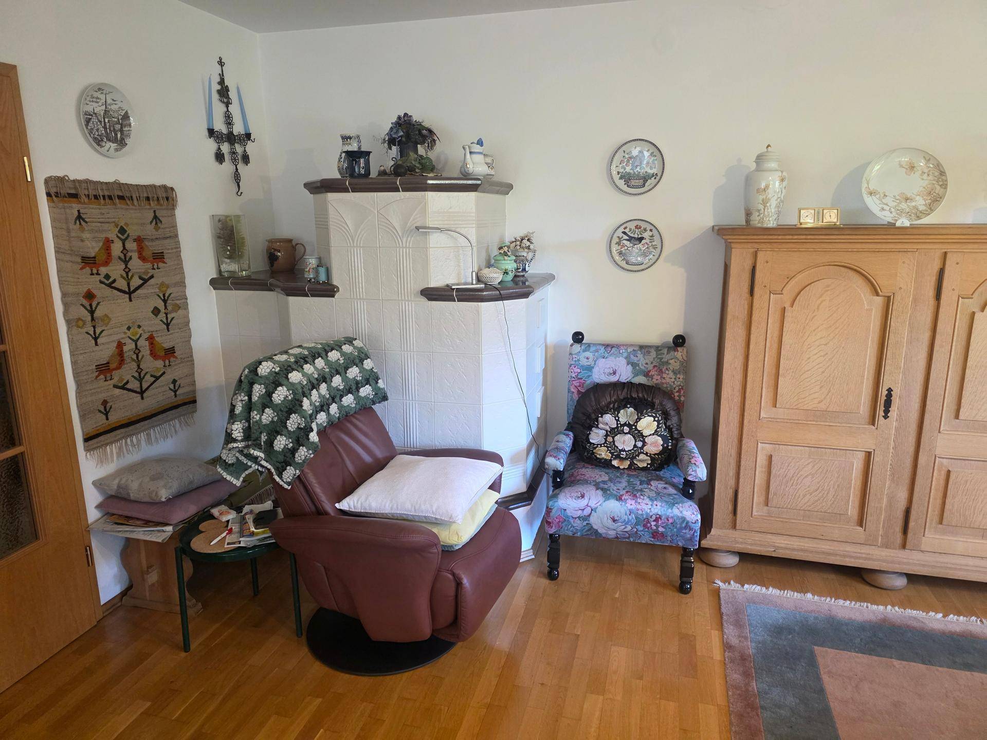 Gemütliche Ecke im Wohnzimmer mit traditionellem Kachelofen und Holzschrank.